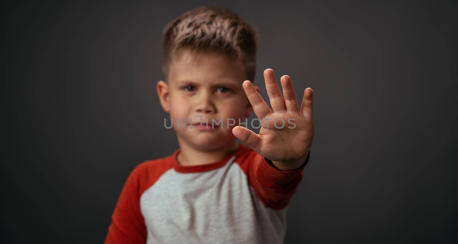 Little boy in red shirt unhappy showing stop with his hand isolated on grey background. Human emotions, facial expression concept. Facial expressions, emotions, feelings.