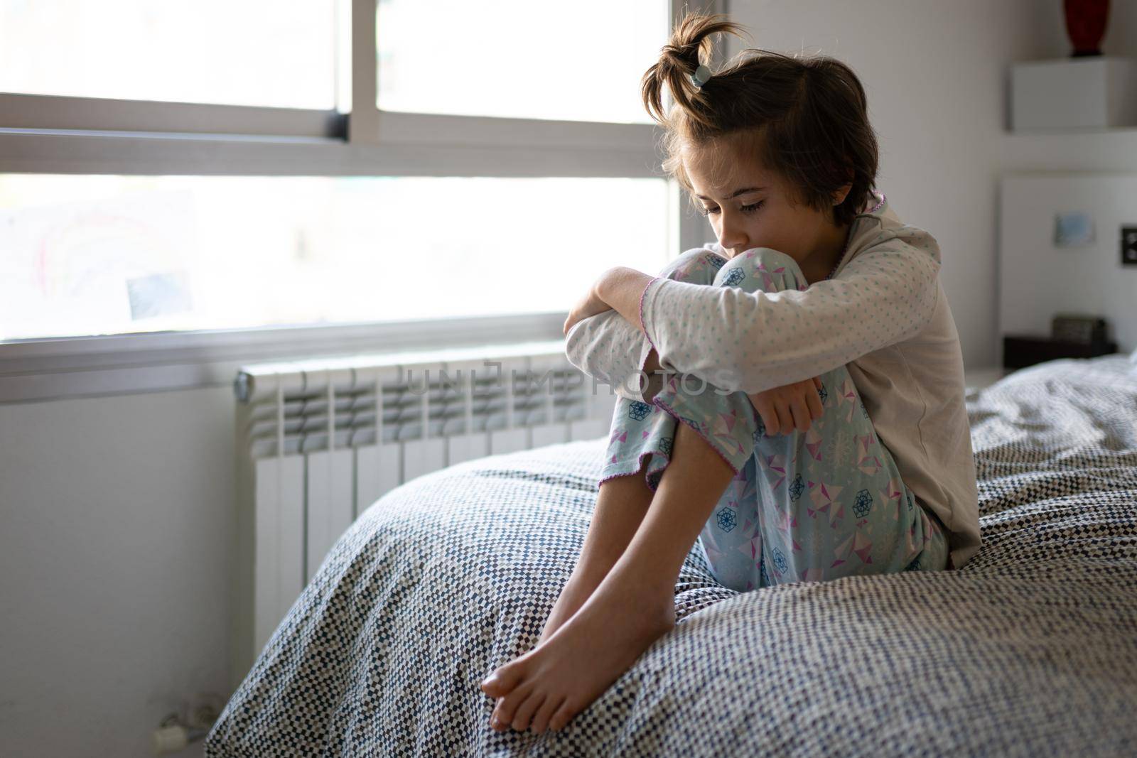Nine-year-old girl sitting in bed at home bored by confinement