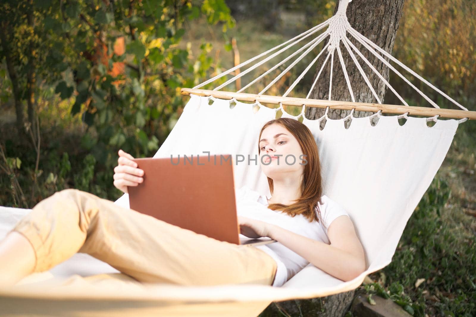 woman outdoors with laptop lies in hammock leisure technology by Vichizh