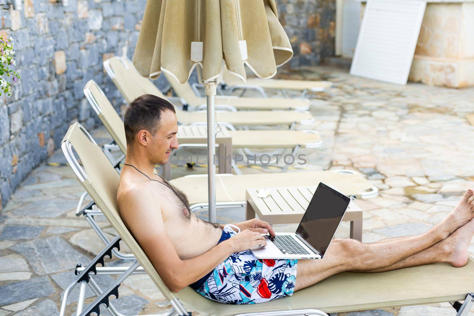 man using a laptop near the pool by Andelov13