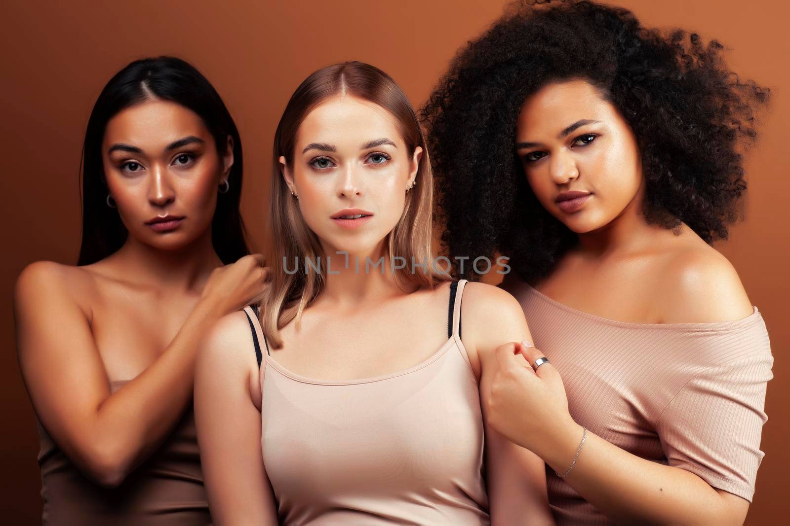 young pretty asian, caucasian, afro woman posing cheerful together on brown background, lifestyle diverse nationality people concept closeup