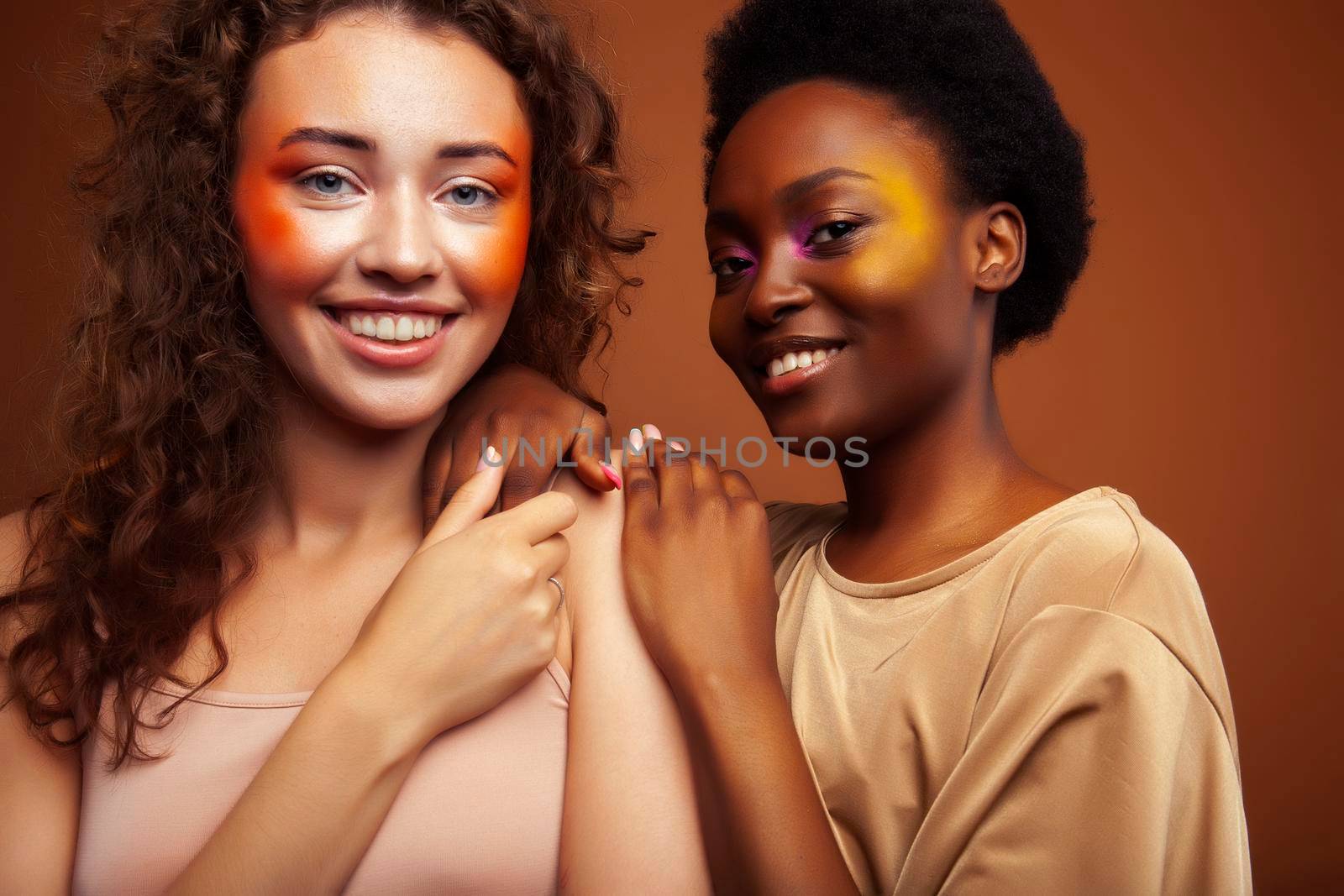 two pretty girls african and caucasian blond posing cheerful together on brown background, ethnicity diverse lifestyle people concept by JordanJ
