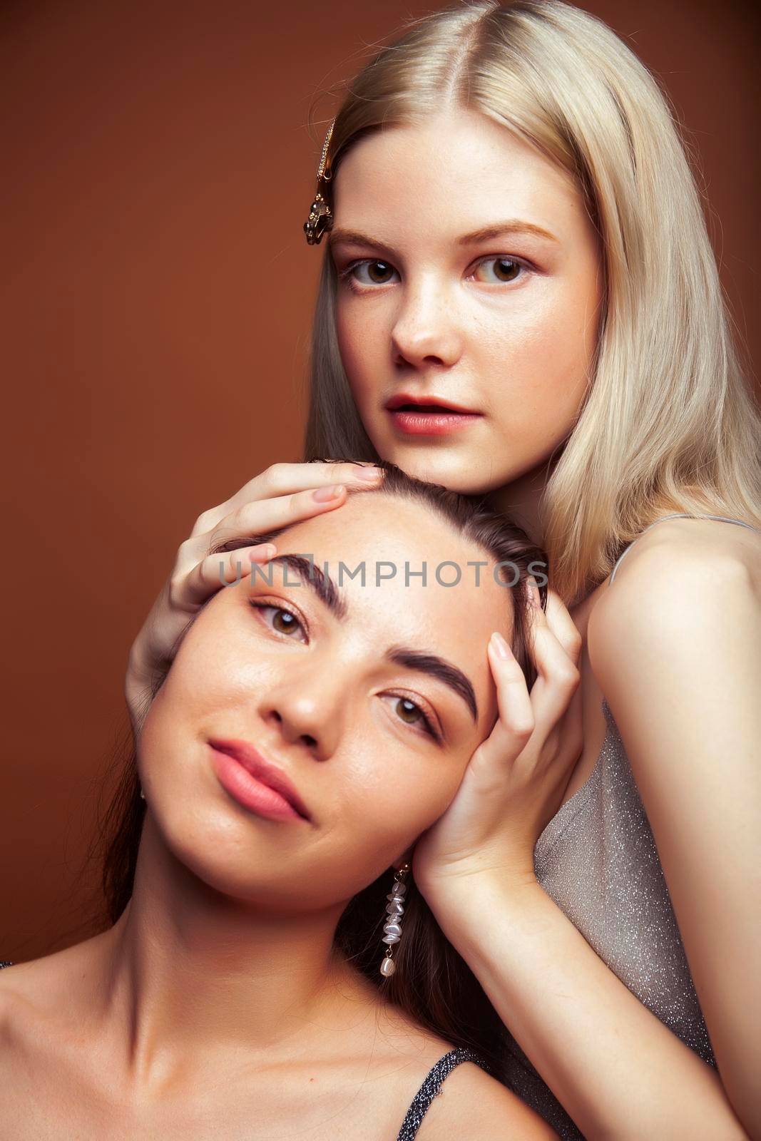 two pretty diverse girls happy posing together: blond and brunette on brown background, lifestyle people concept by JordanJ