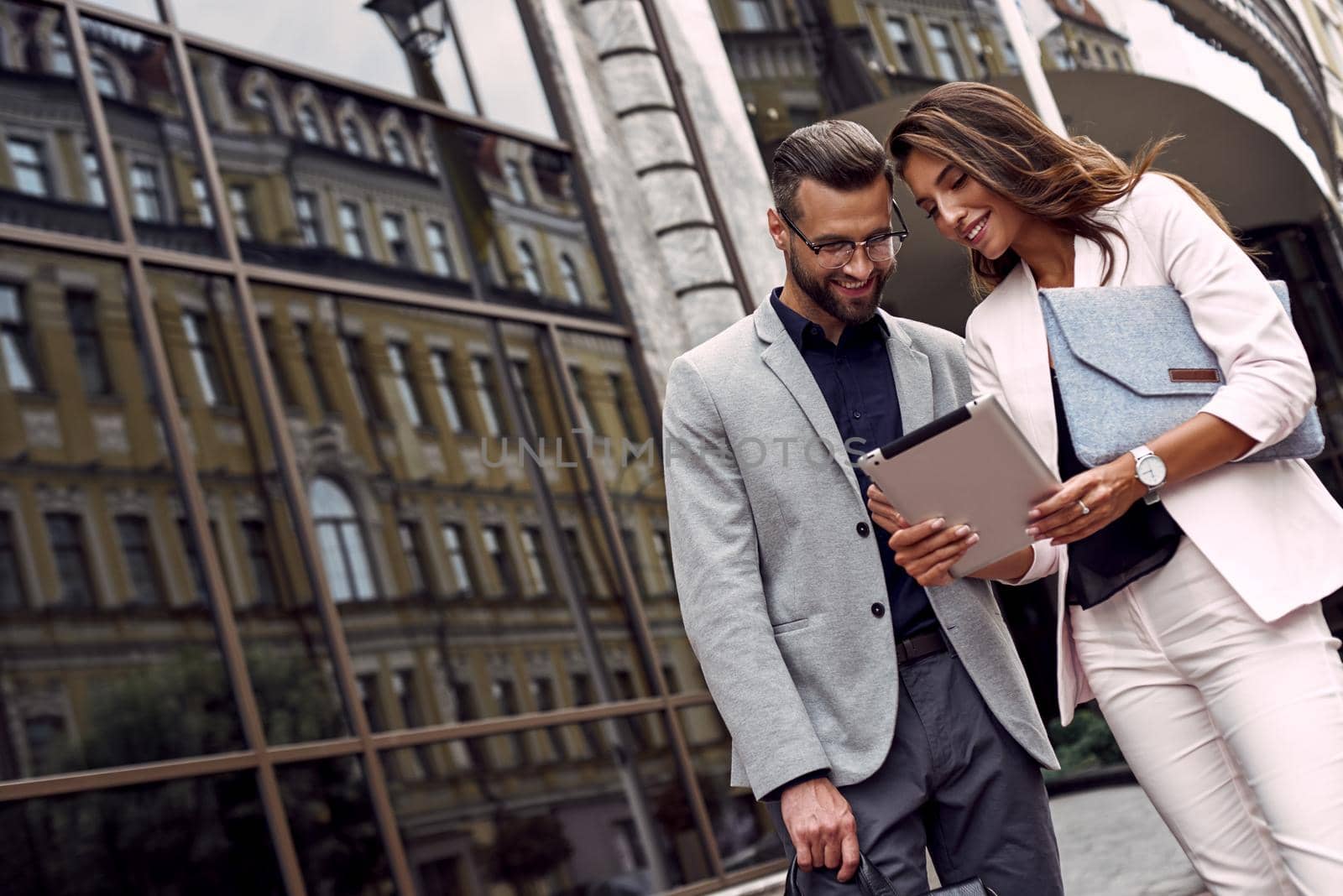 Using gadget. Two young business people standing outside on the city street using digital tablet checking latest news smiling joyful