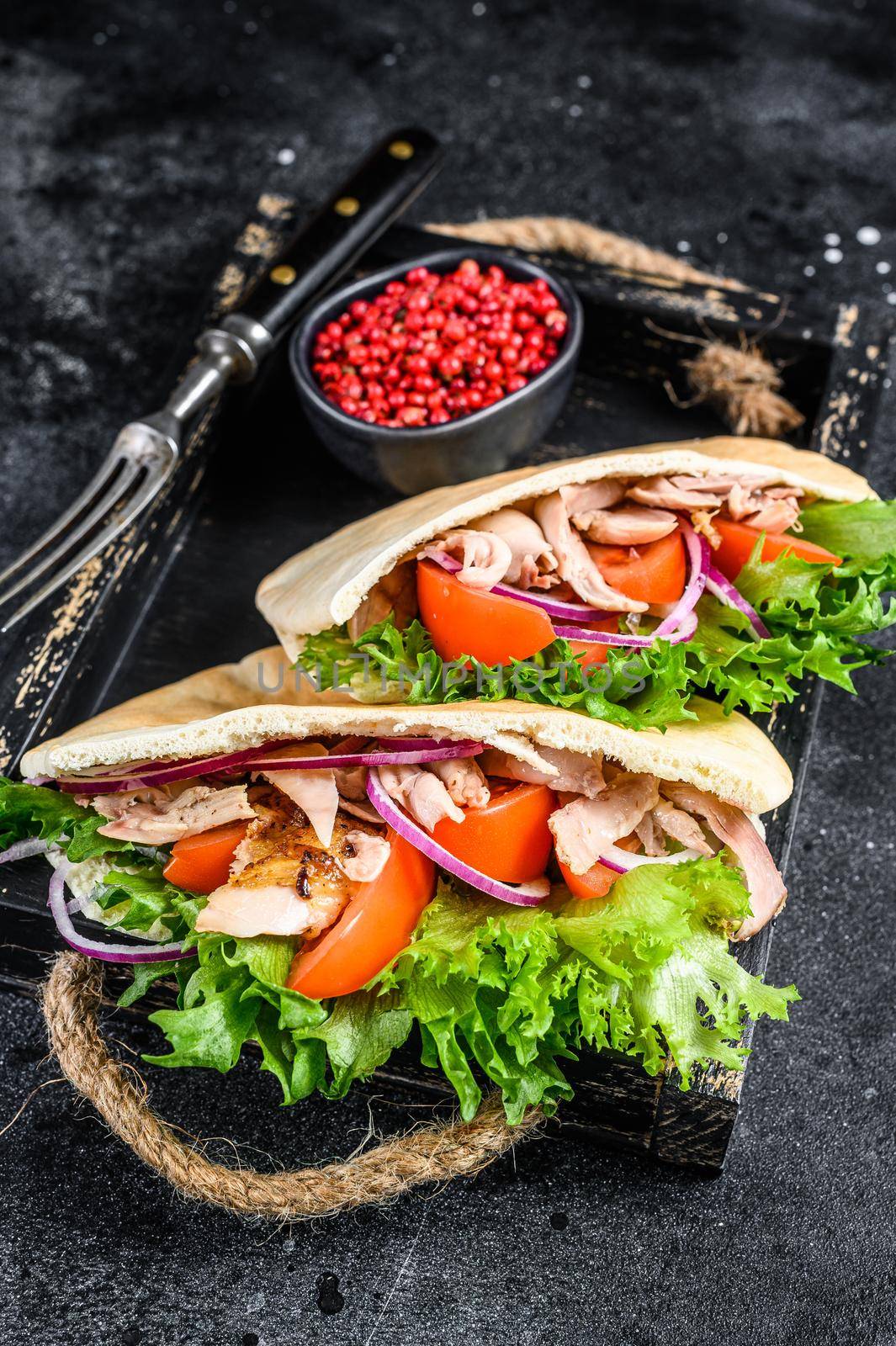 Doner kebab with grilled chicken meat and vegetables in pita bread on a wooden tray. Black background. Top view.