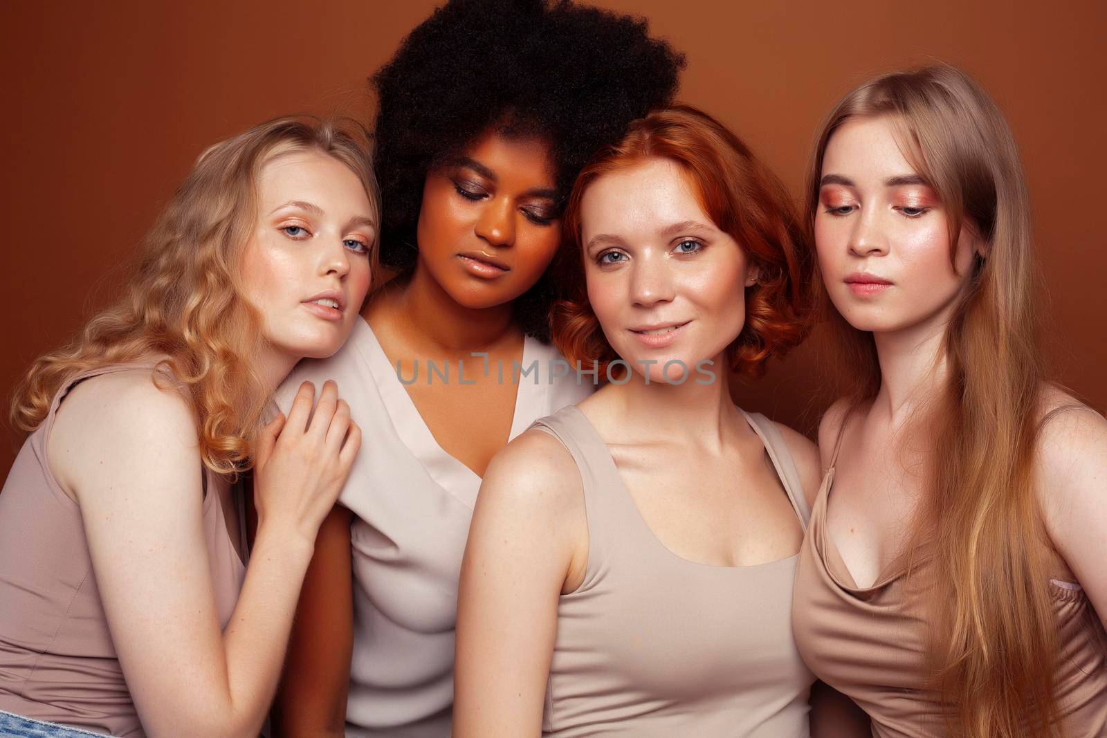 young pretty caucasian, afro, scandinavian woman posing cheerful together on brown background, lifestyle diverse nationality people concept close up