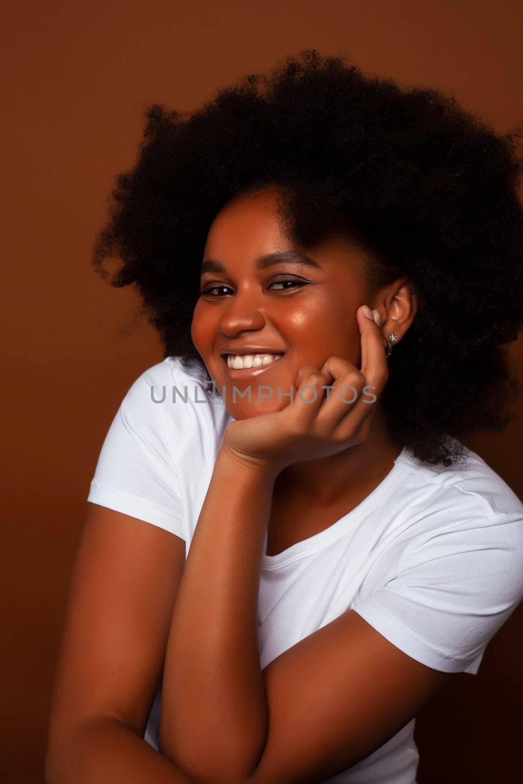pretty young african american woman with curly hair posing cheerful gesturing on brown background, lifestyle people concept by JordanJ