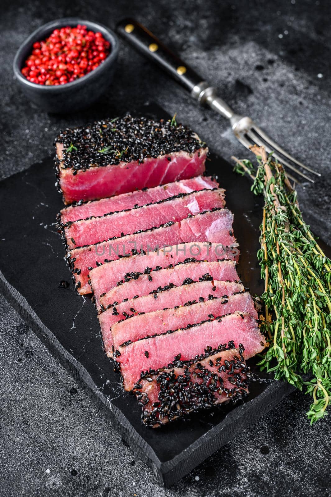 Rare Ahi tuna steak slices with fresh herbs on a cutting board. Black background. Top view.