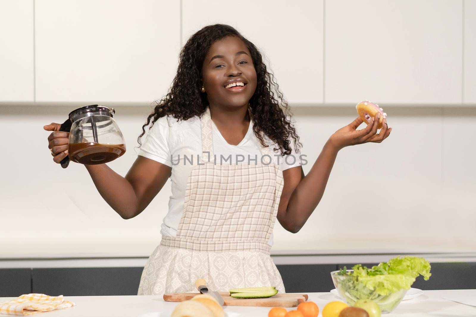 Smiling African Lady has black coffee and a Donut for a snack. Coffee and Sweets for Breakfast. Close-up. High quality photo