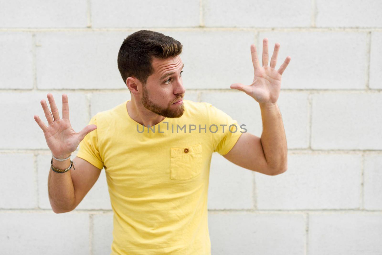 Funny young man on brick wall with open hands looking at rightside. Guy wearing casual clothes in urban background.