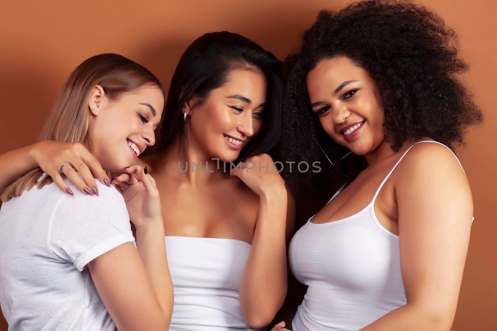 young pretty asian, caucasian, afro woman posing cheerful together on brown background, lifestyle diverse nationality people concept closeup