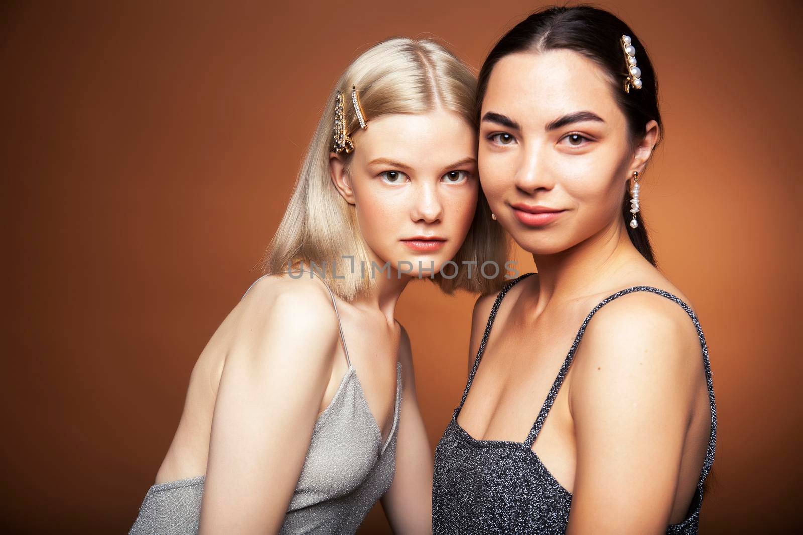 two pretty diverse girls happy posing together: blond and brunette on brown background, lifestyle people concept closeup