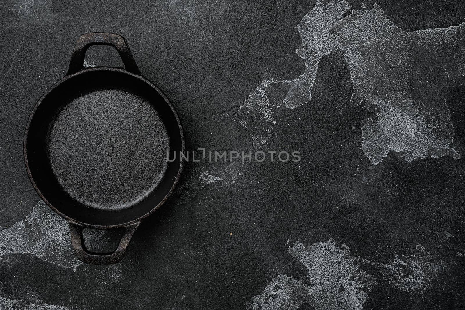 Cast iron frying pan set with copy space for text or food with copy space for text or food, top view flat lay, on black dark stone table background