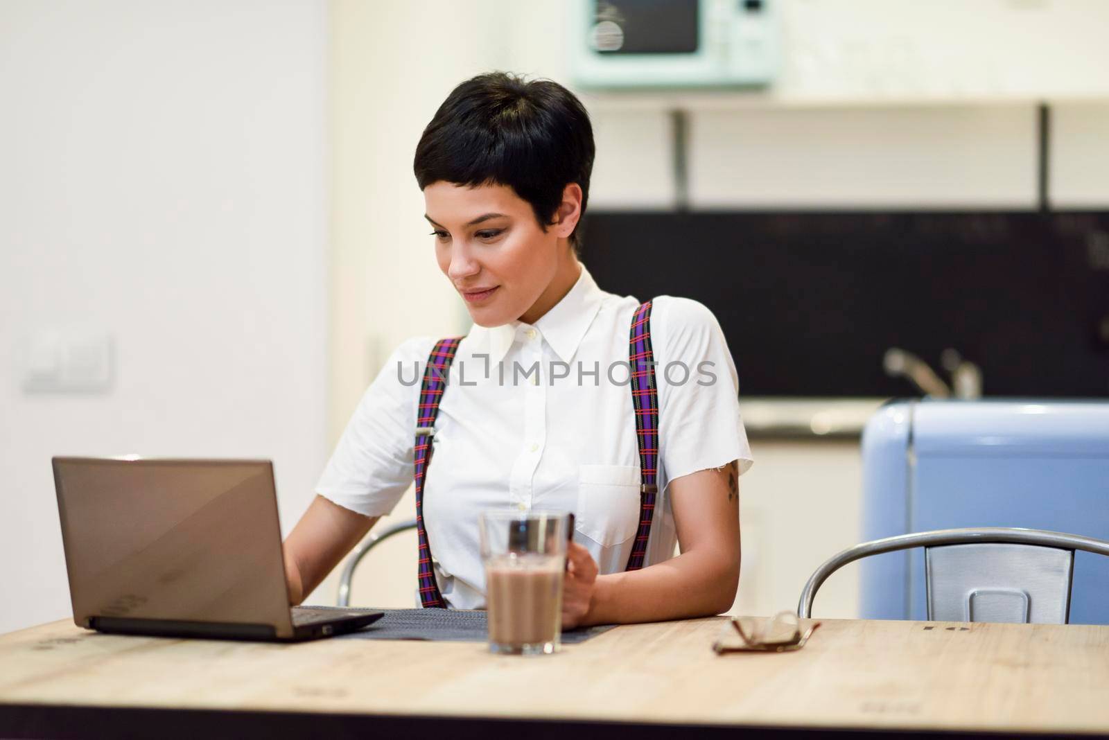 Young woman with very short haircut typing with a laptop at home. Businesswoman working at home concept.