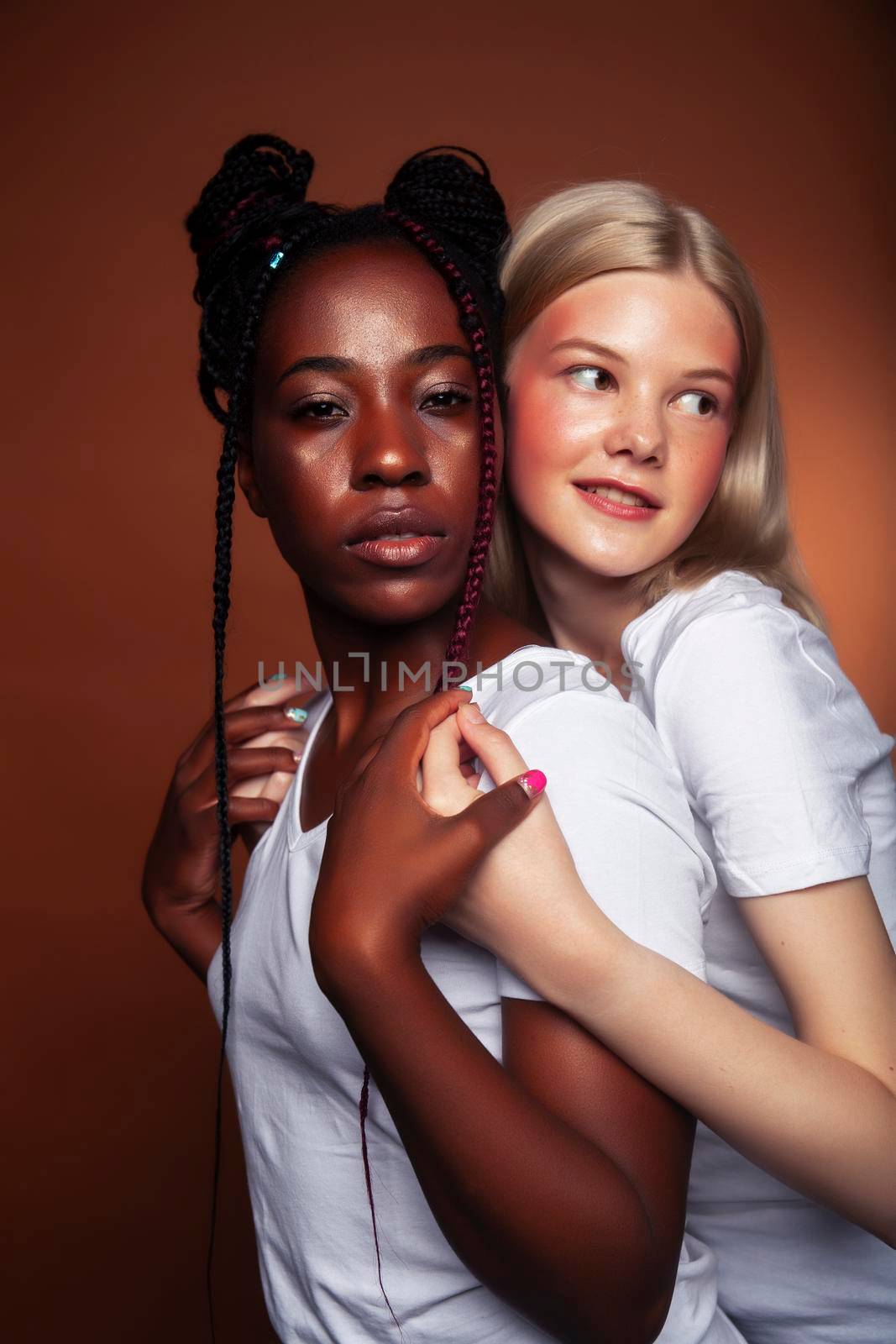 two pretty girls african and caucasian blond posing cheerful together on brown background, ethnicity diverse lifestyle people concept close up