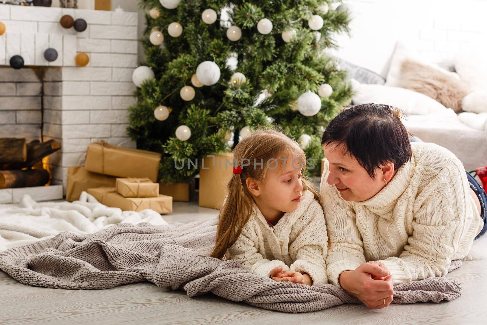 Mother and daughter unwrapping a present lying on the floor in the living room by Andelov13