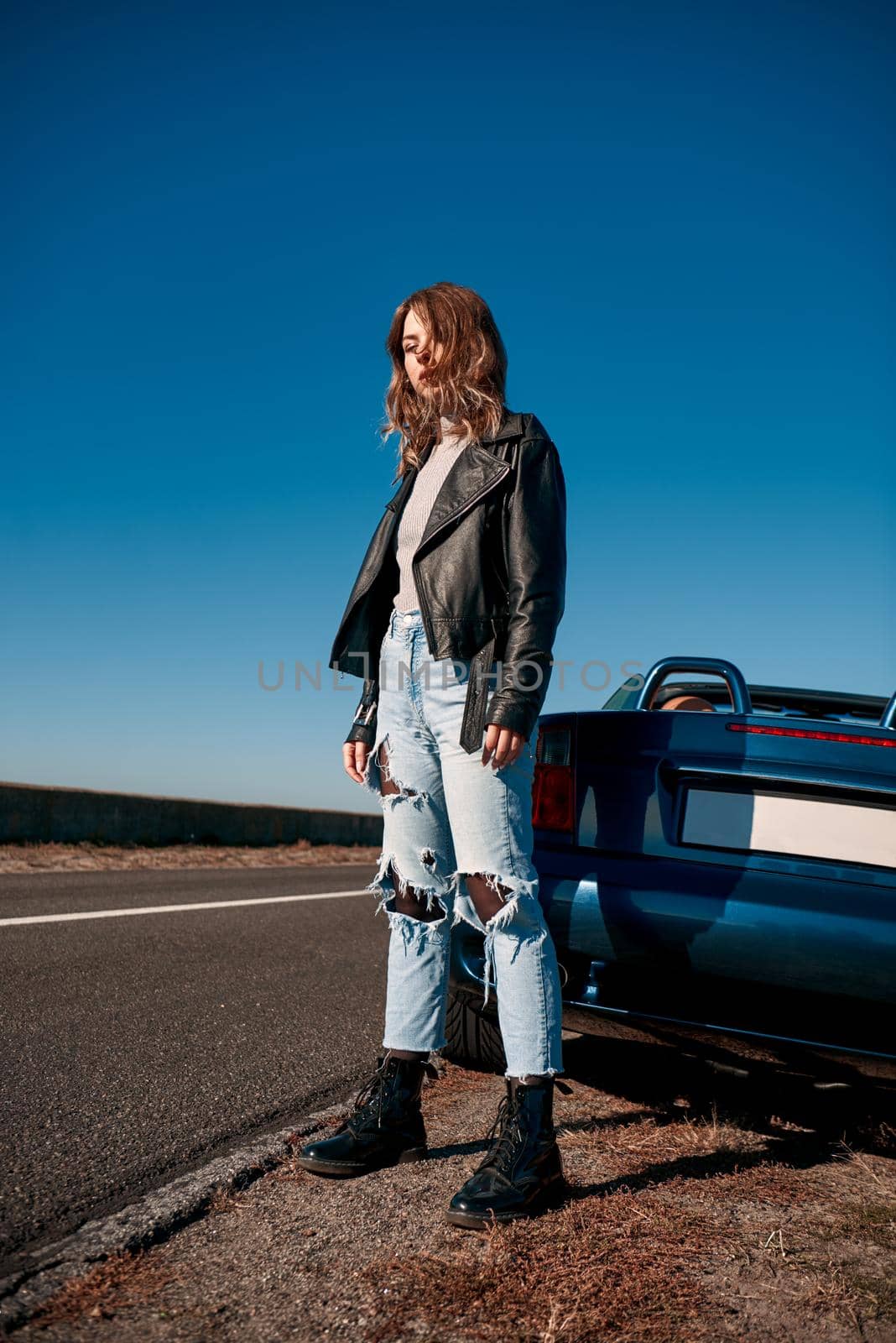 Young woman standing near roofless car in leather jacket by friendsstock