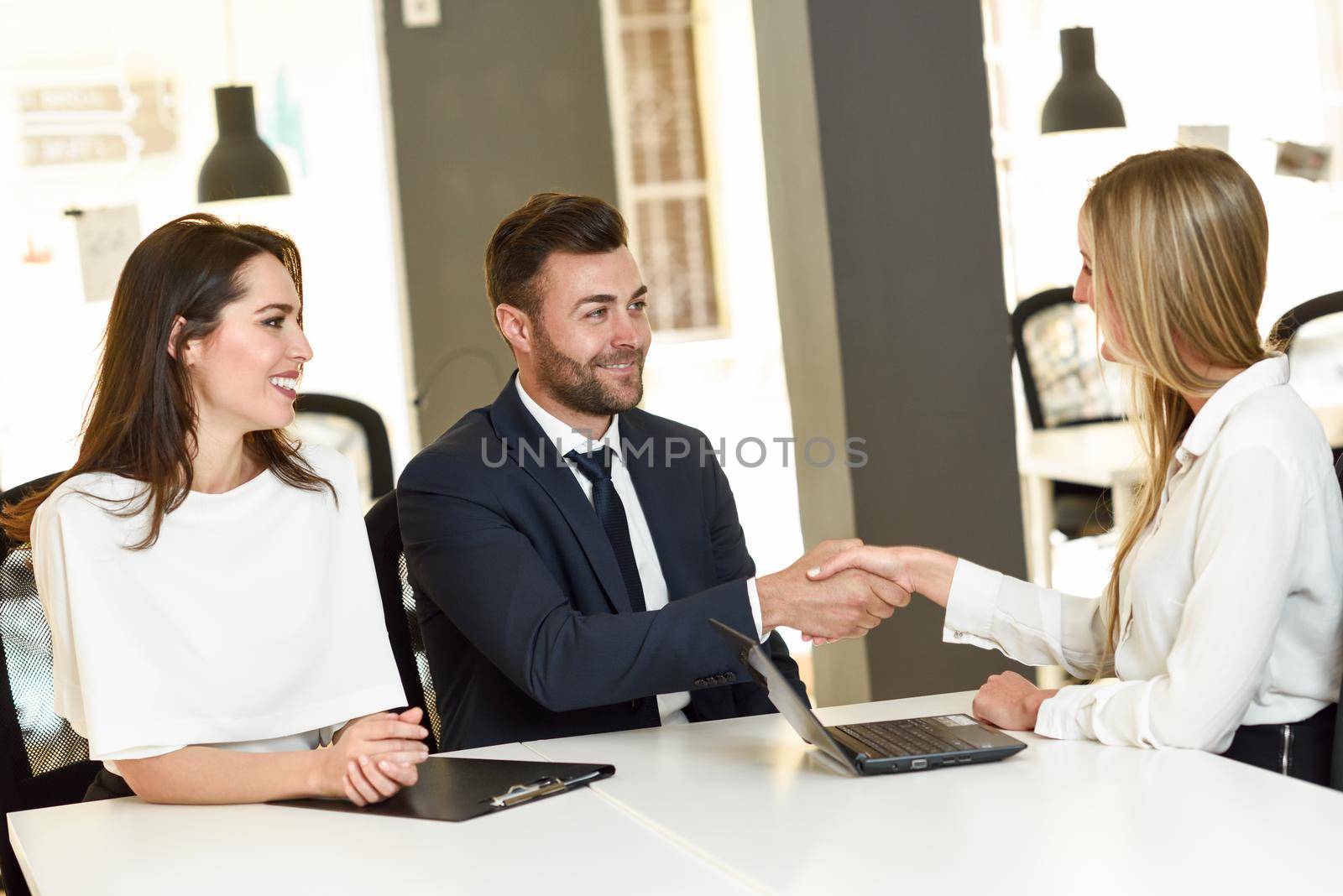 Smiling young couple shaking hands with an insurance agent or investment adviser. Three people meeting in an office reaching an agreement