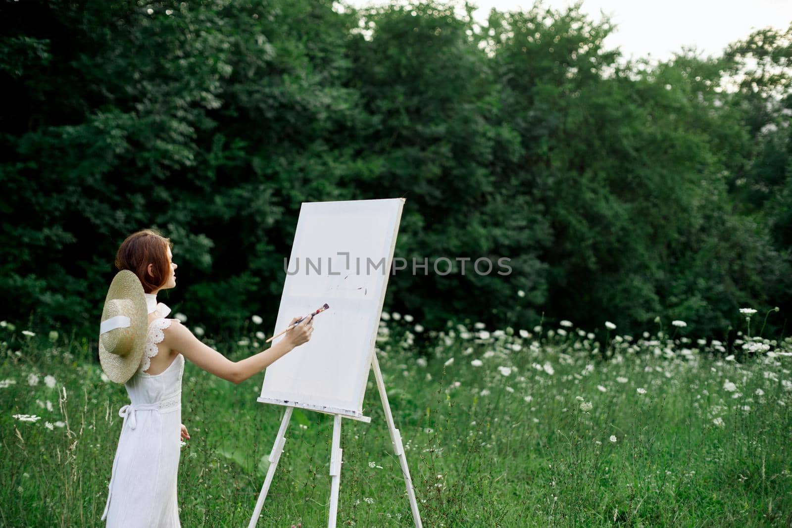 Woman in white dress paints a picture outdoors hobby creative. High quality photo