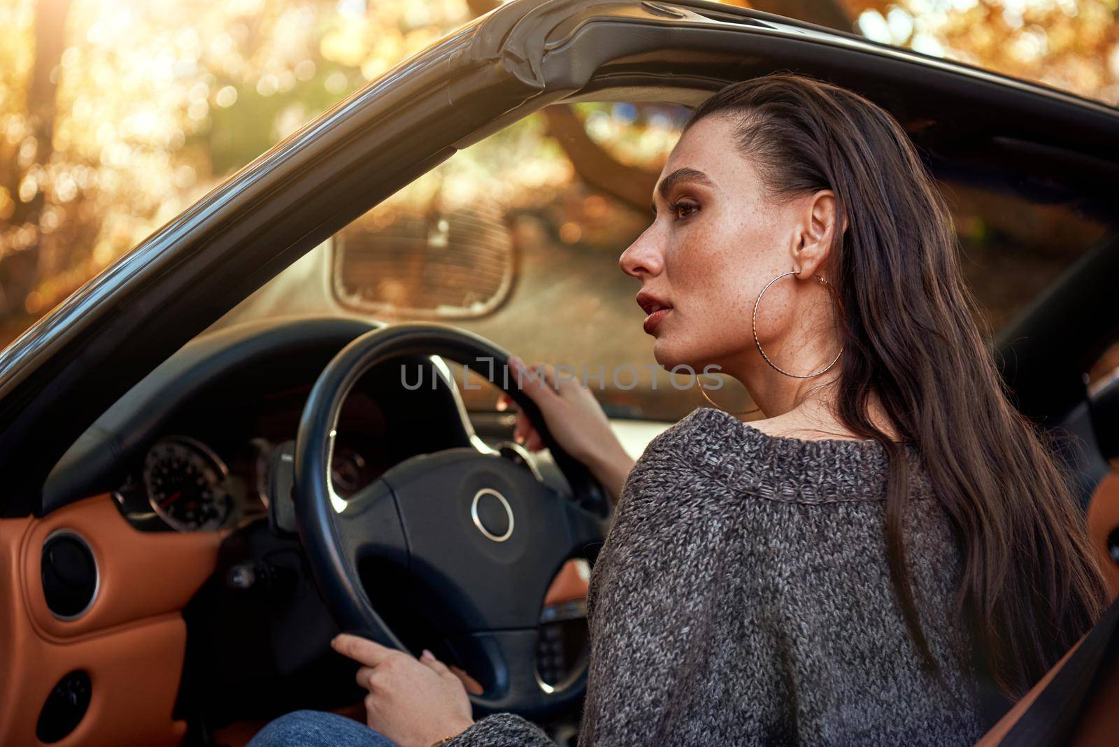 Sexy young woman in jeans and in a grey sweater sits in a cabriolet by friendsstock