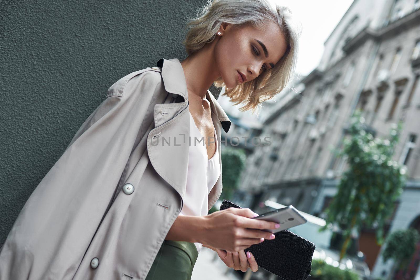 Fashion. Young stylish woman standing on the city street using application on smartphone concentrated close-up by friendsstock