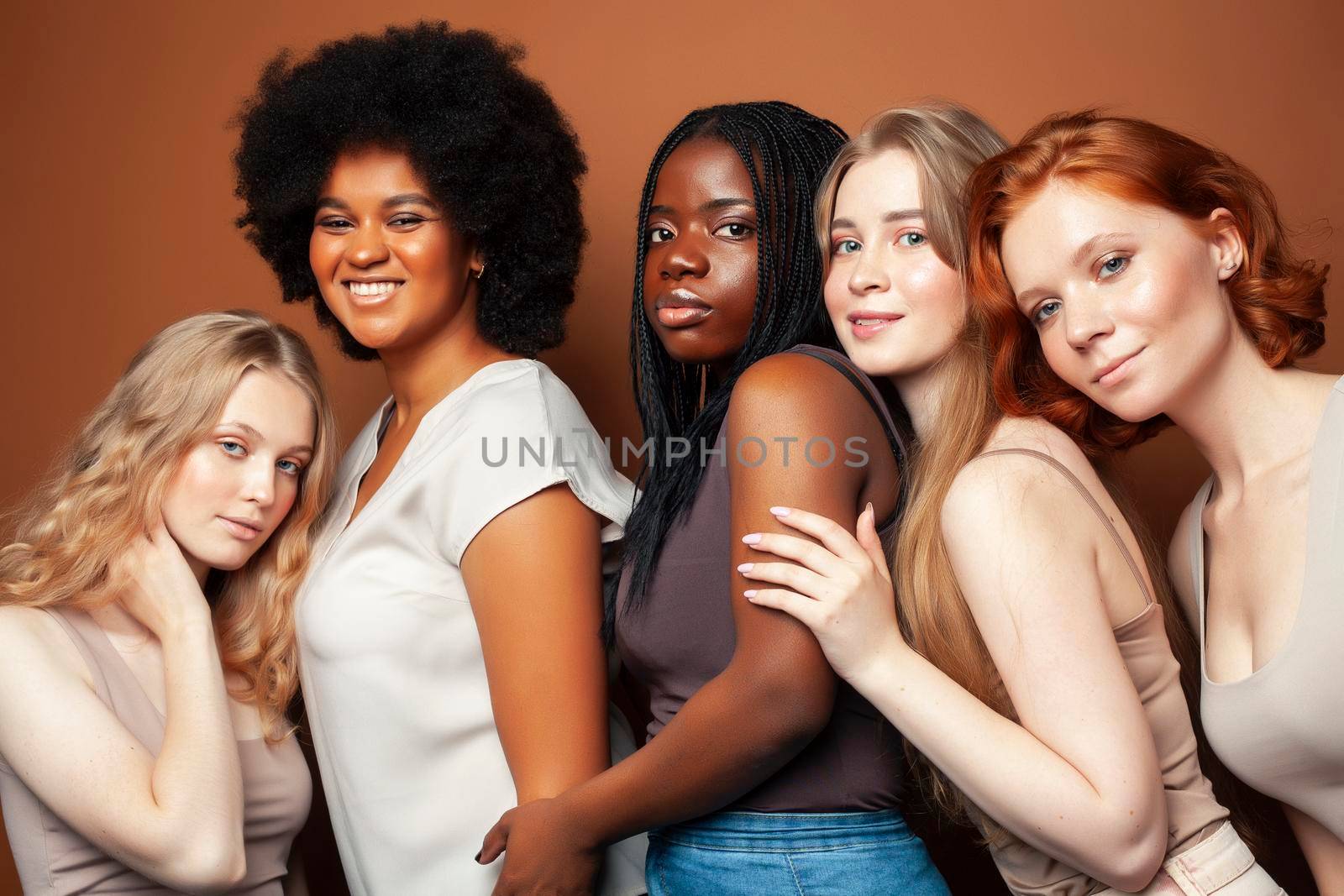 young pretty african and caucasian women posing cheerful together on brown background, lifestyle diverse nationality people concept closeup