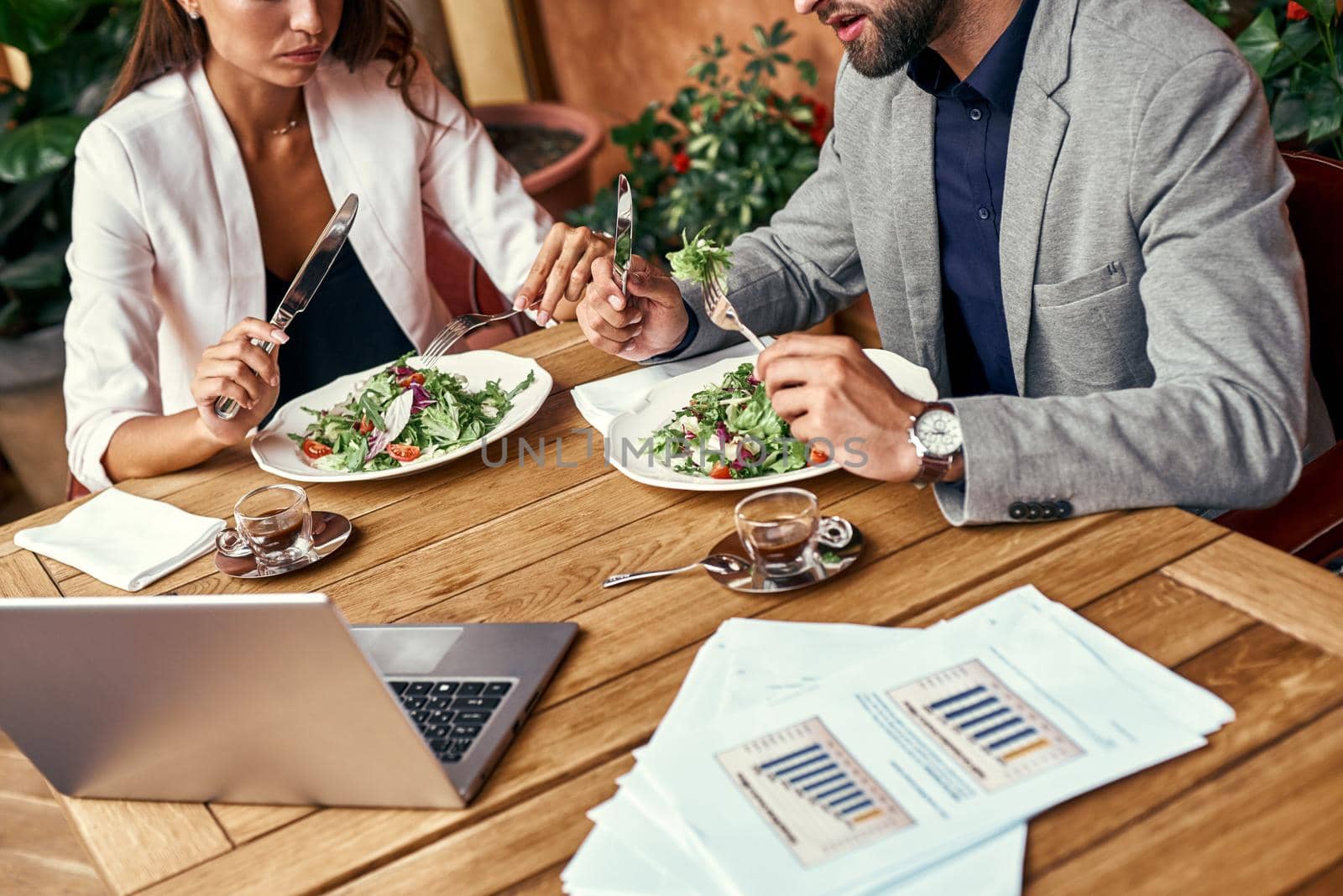 Business lunch. Man and woman sitting at table at restaurant eating healthy fresh salad discussing project close-up by friendsstock