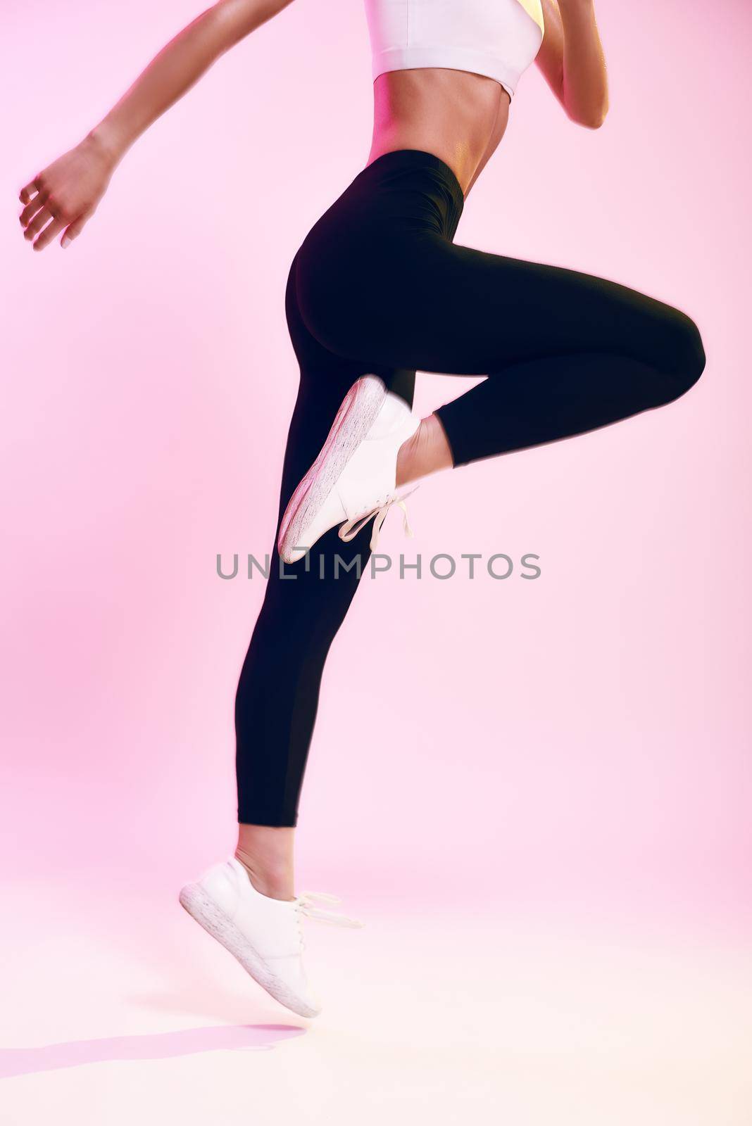 Never stop Cropped photo of sporty young woman in black leggings jumping against pink background in studio. Sport. Active lifestyle. Studio shot