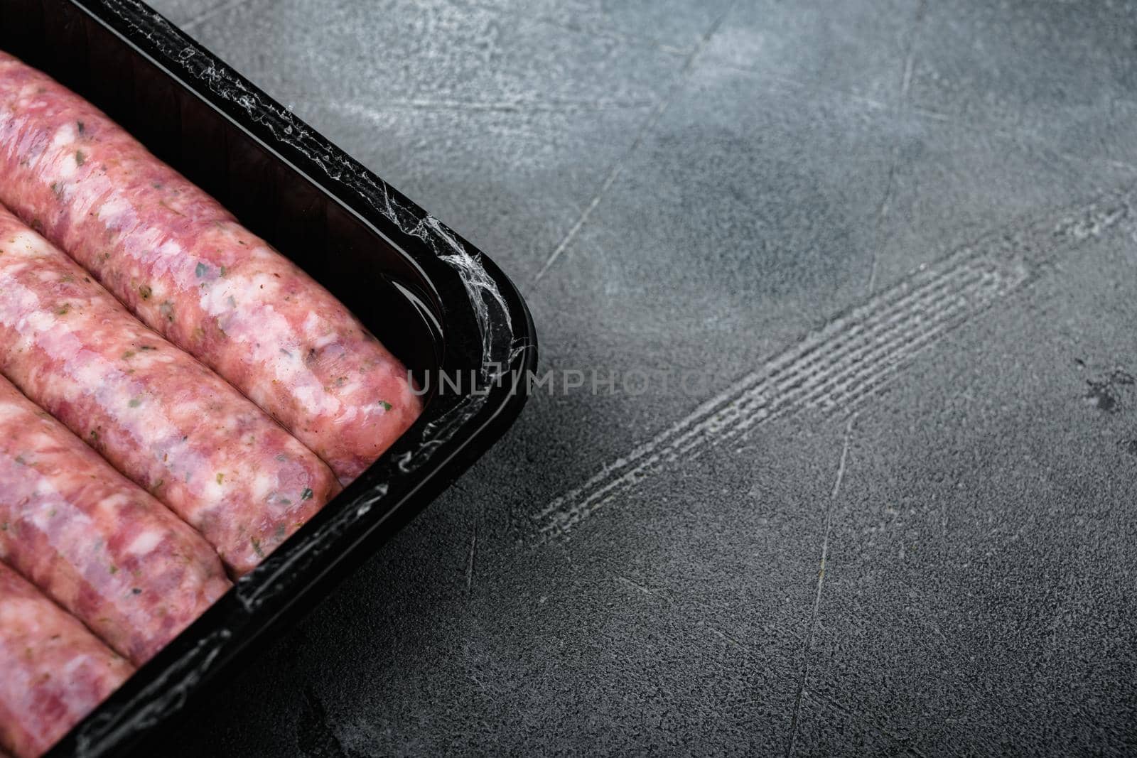 Uncooked meat sausages in plastic pack set, on gray stone table background, with copy space for text