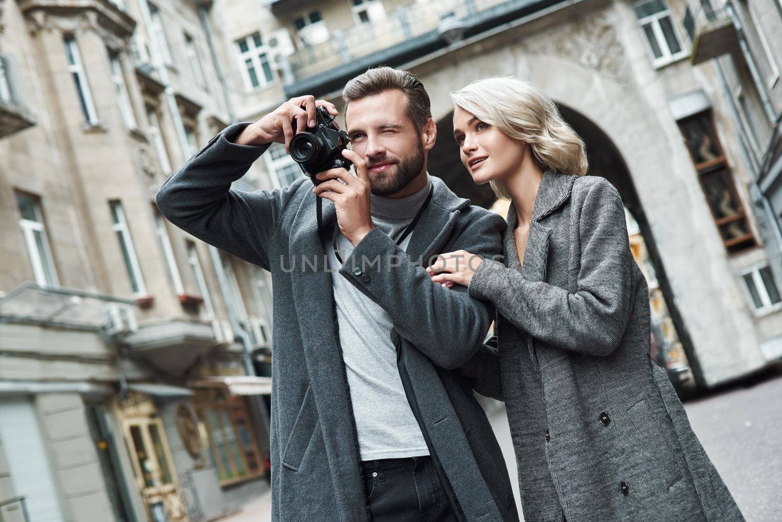 Romantic date outdoors. Young couple walking on the city street taking photos on camera smiling excited by friendsstock