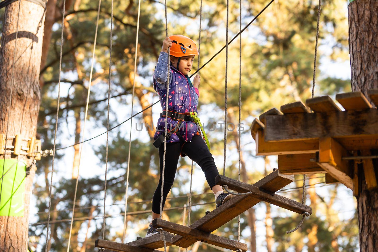 the girl in the orange helmet in the adventure Park holds on to the ropes by Andelov13