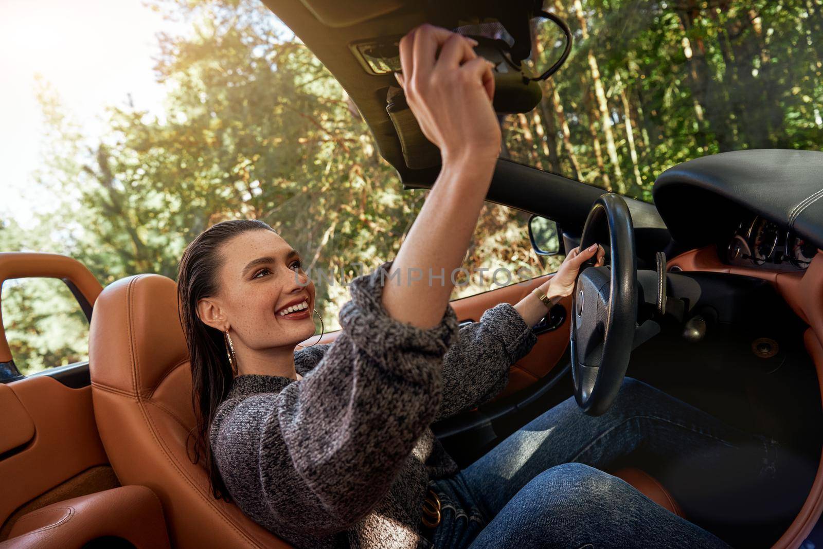 Sexy young woman in jeans and in a grey sweater sits in front seat of a cabriolet. Autumn season