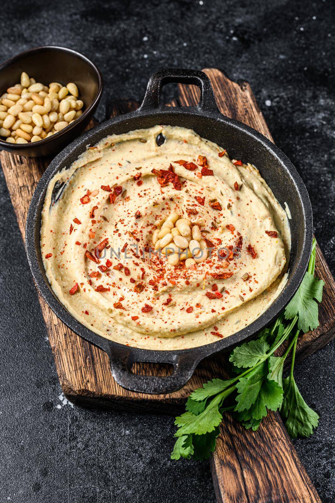 Hummus paste with chickpea and parsley in a bowl. Black background. Top view.