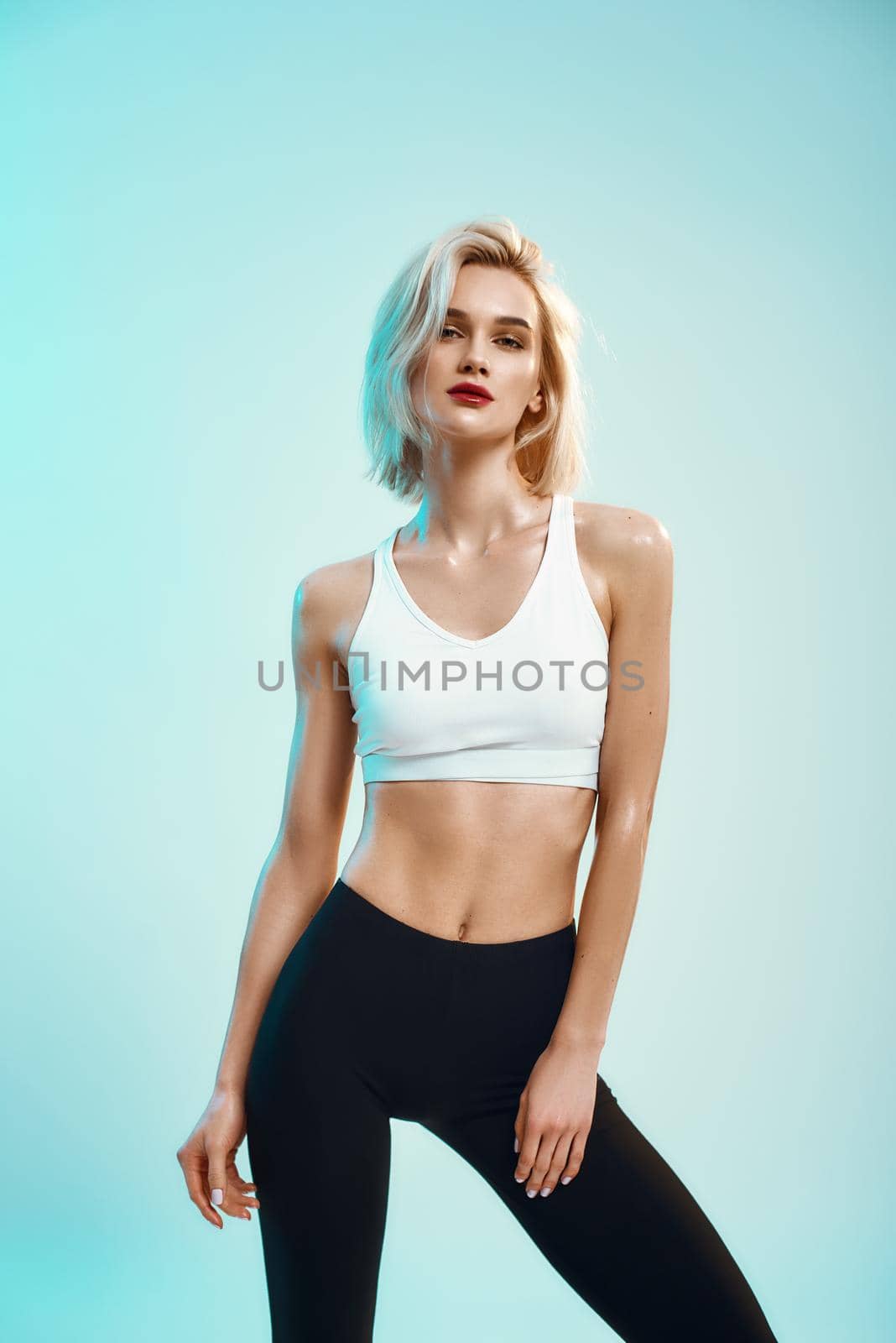 Beauty portrait. Sexy young woman in white top and black leggings looking at camera while standing against blue background in studio by friendsstock