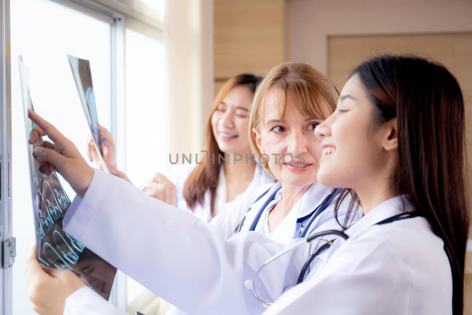 Group of team doctors examining x-ray film about skull and skeleton of patient for checking disease while discussion at hospital, doctors and assistant talking and conference, medical concept.