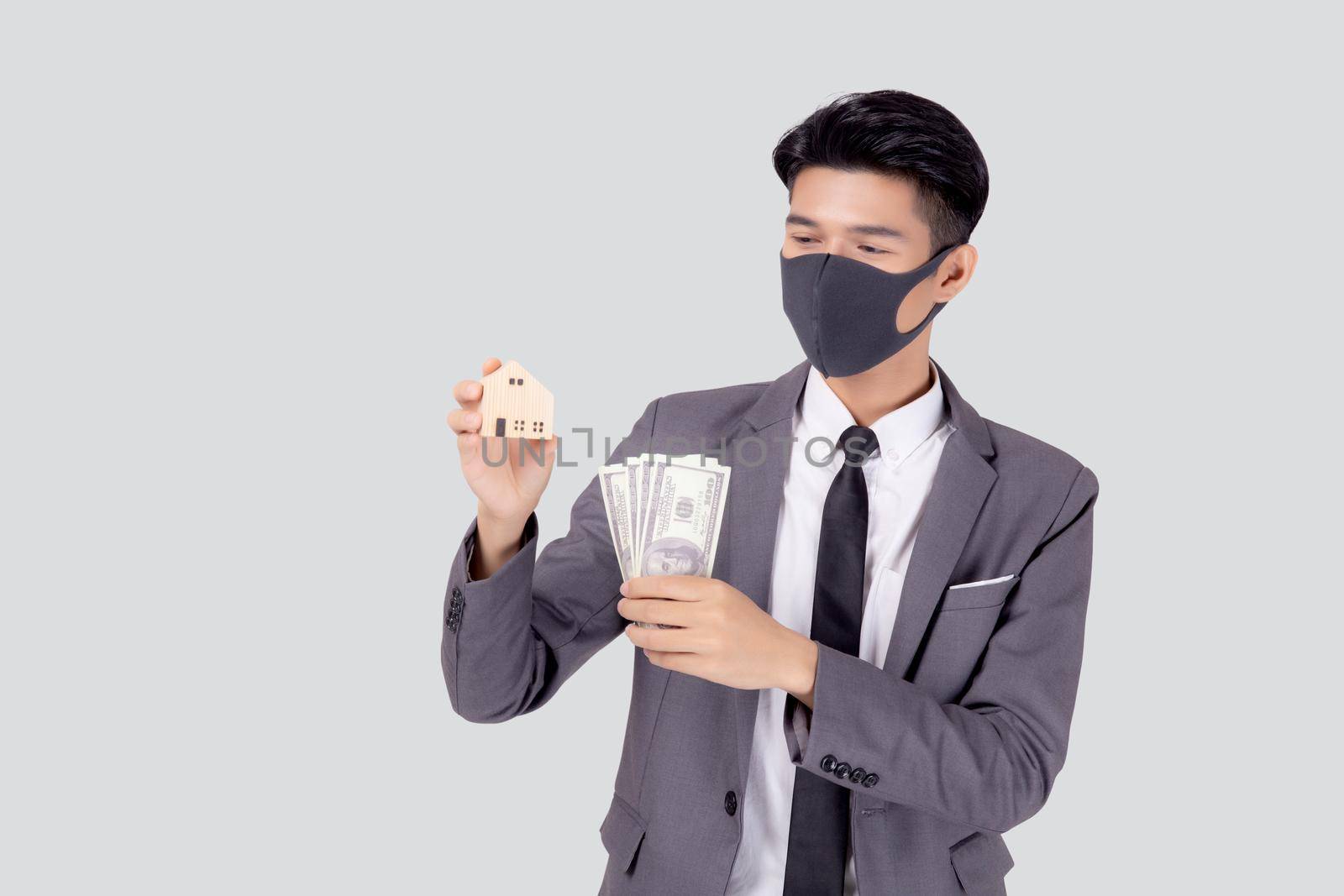 Young asian businessman in face mask holding money dollar and home isolated on white background, pandemic and crisis of economic, business man and investment property during disease covid-19. by nnudoo