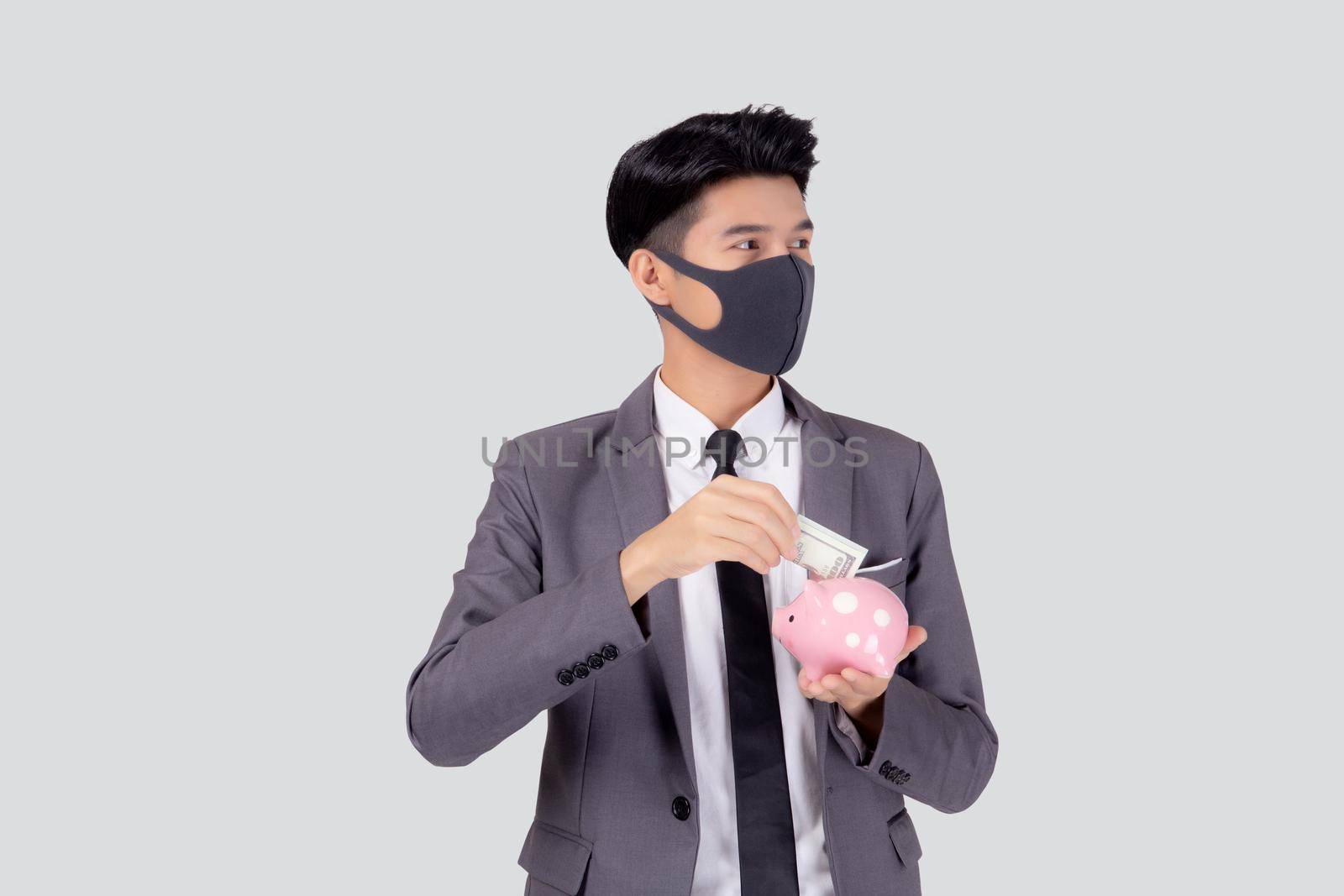 Young asian businessman in face mask holding money dollar and piggy bank isolated on white background, crisis of economic, business man in mask investment finance and saving during disease covid-19. by nnudoo