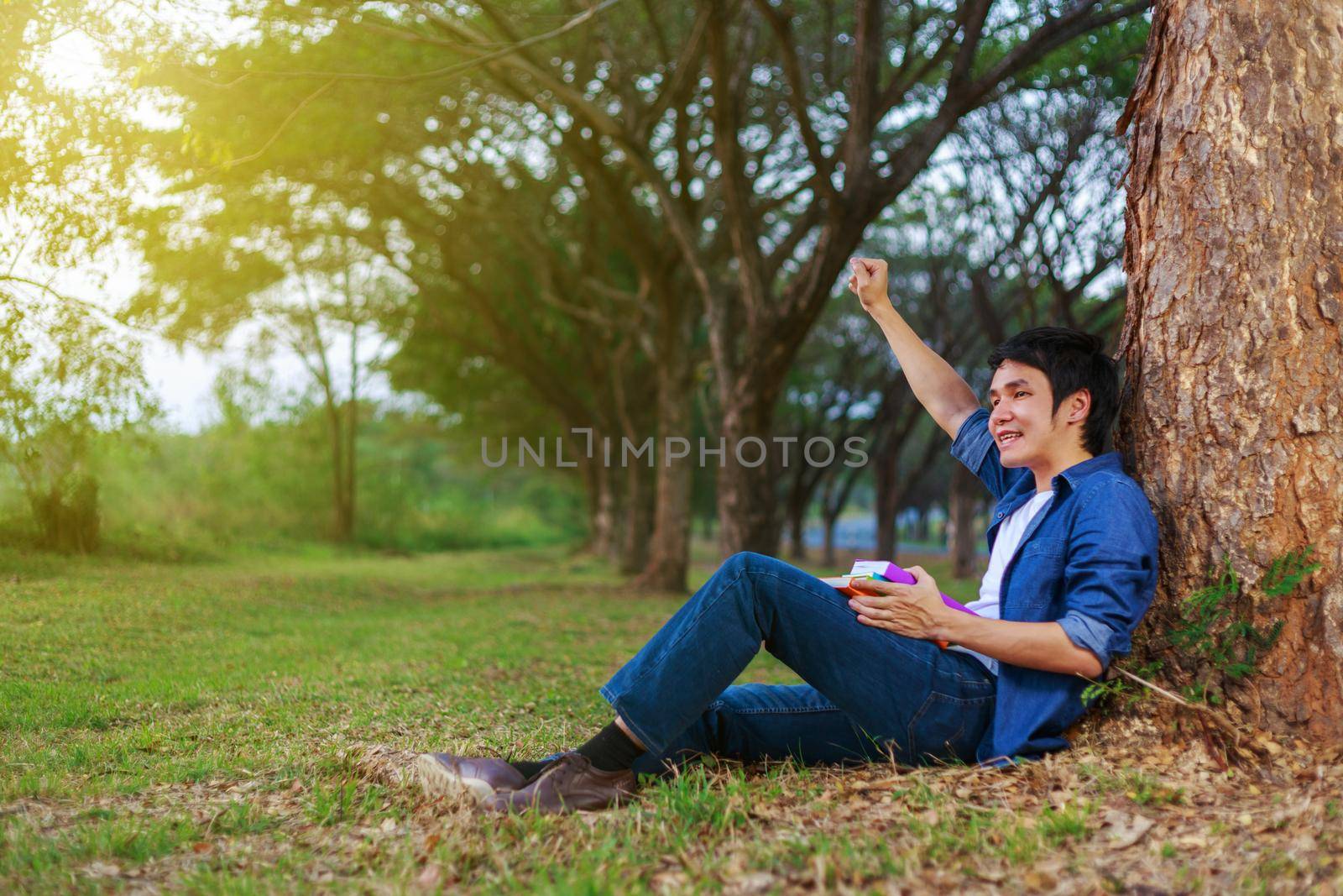 cheerful man  holding a book with arm raised in the park