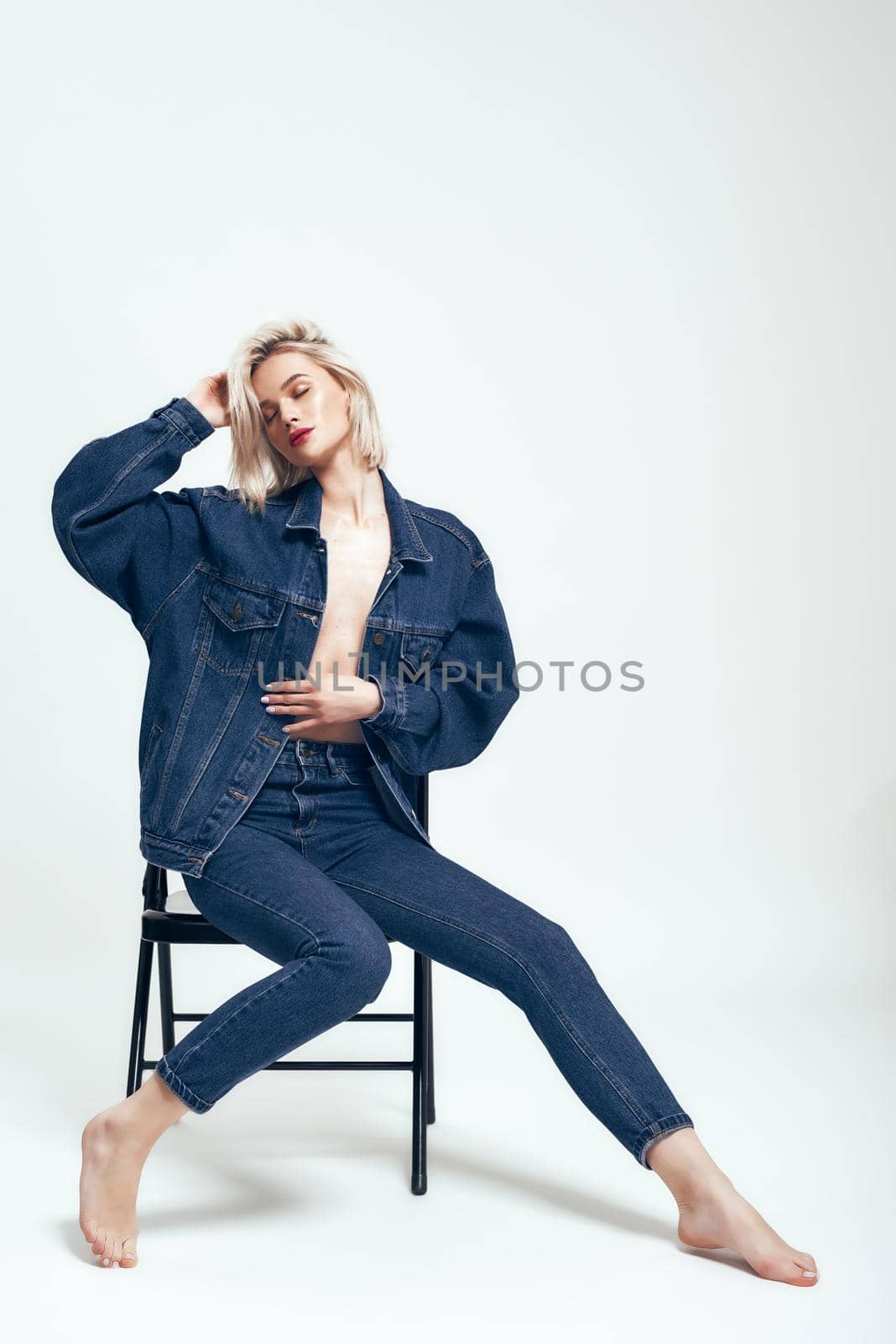 Trendy look. Full length of attractive young woman in jeans wear keeping eyes closed while sitting on the chair against grey background in studio by friendsstock