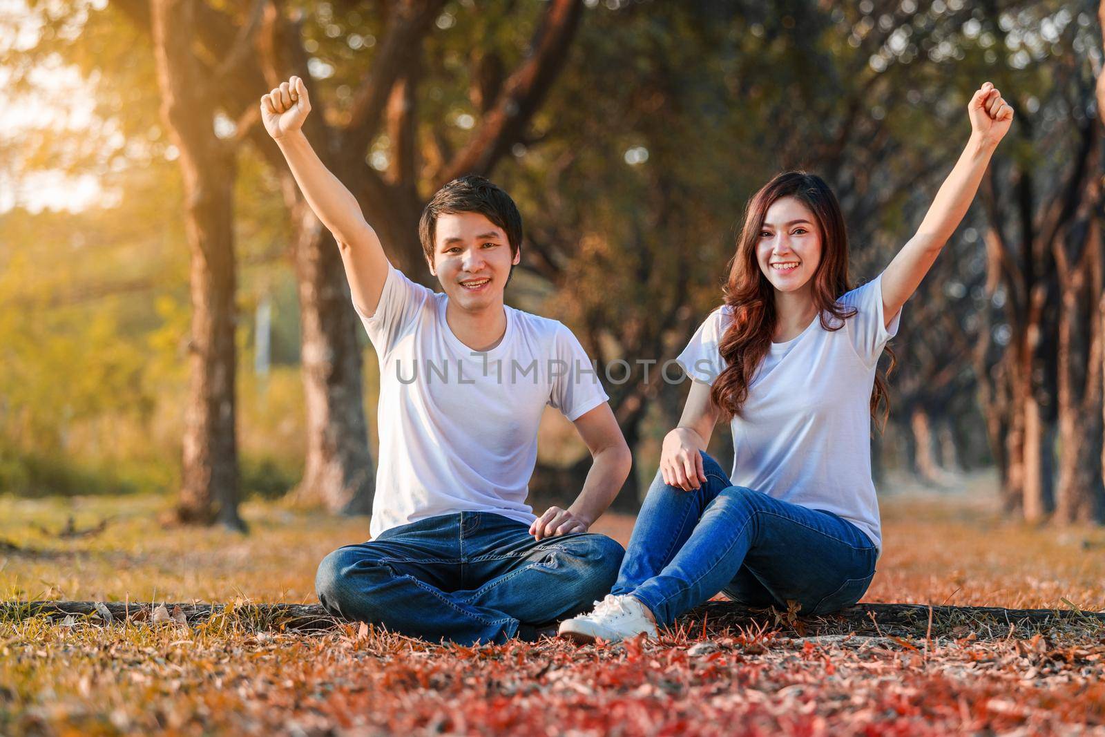 happy young couple with arm raised in park  by geargodz