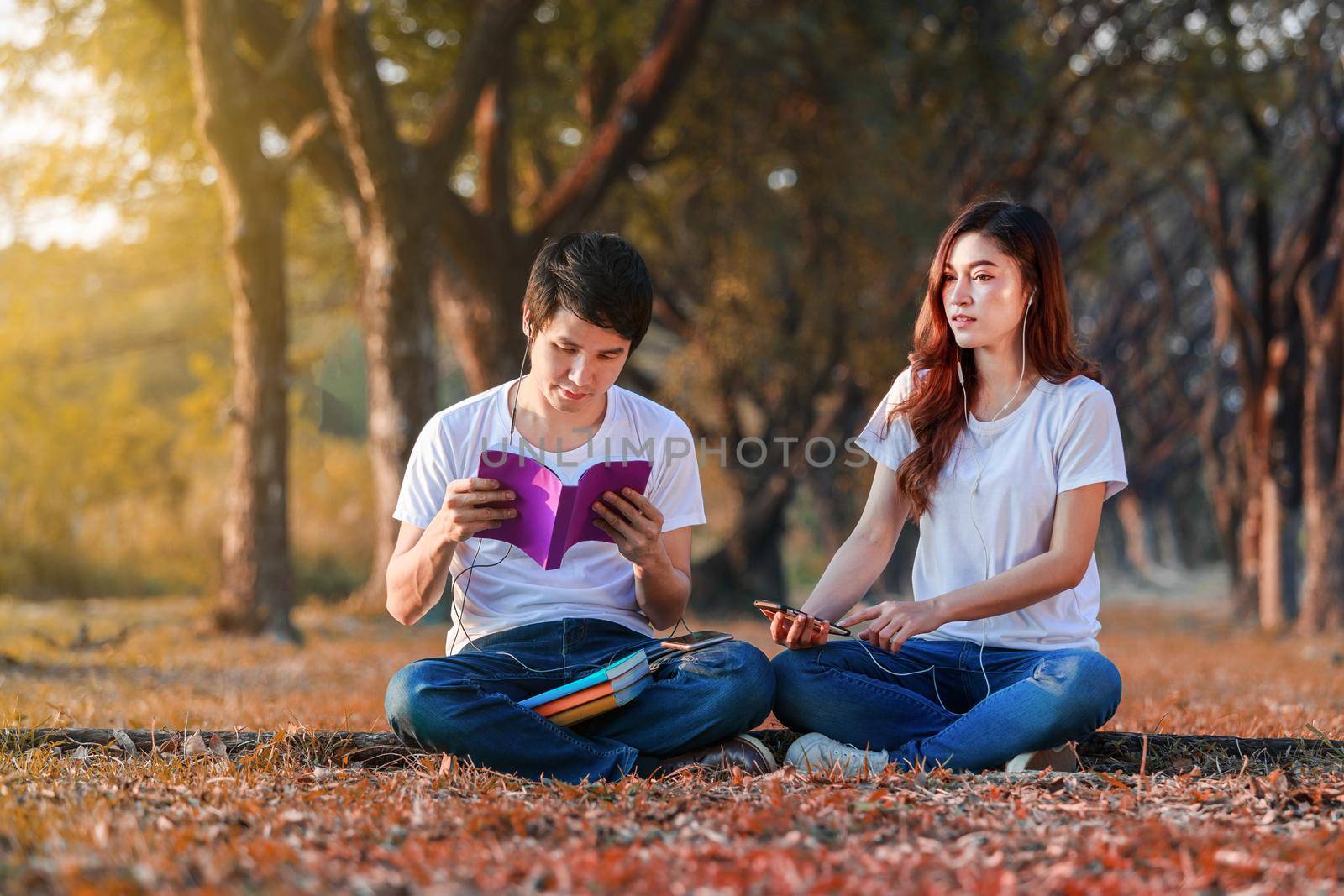 young couple reading a book and listening music with earphones in park by geargodz