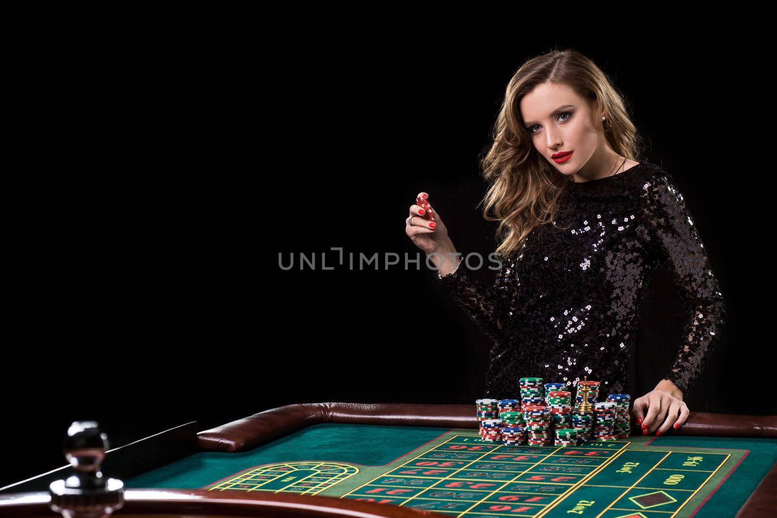 Sexy woman in a black dress playing in casino. Woman stakes piles of chips playing roulette at the casino club. Gambling. Roulette.