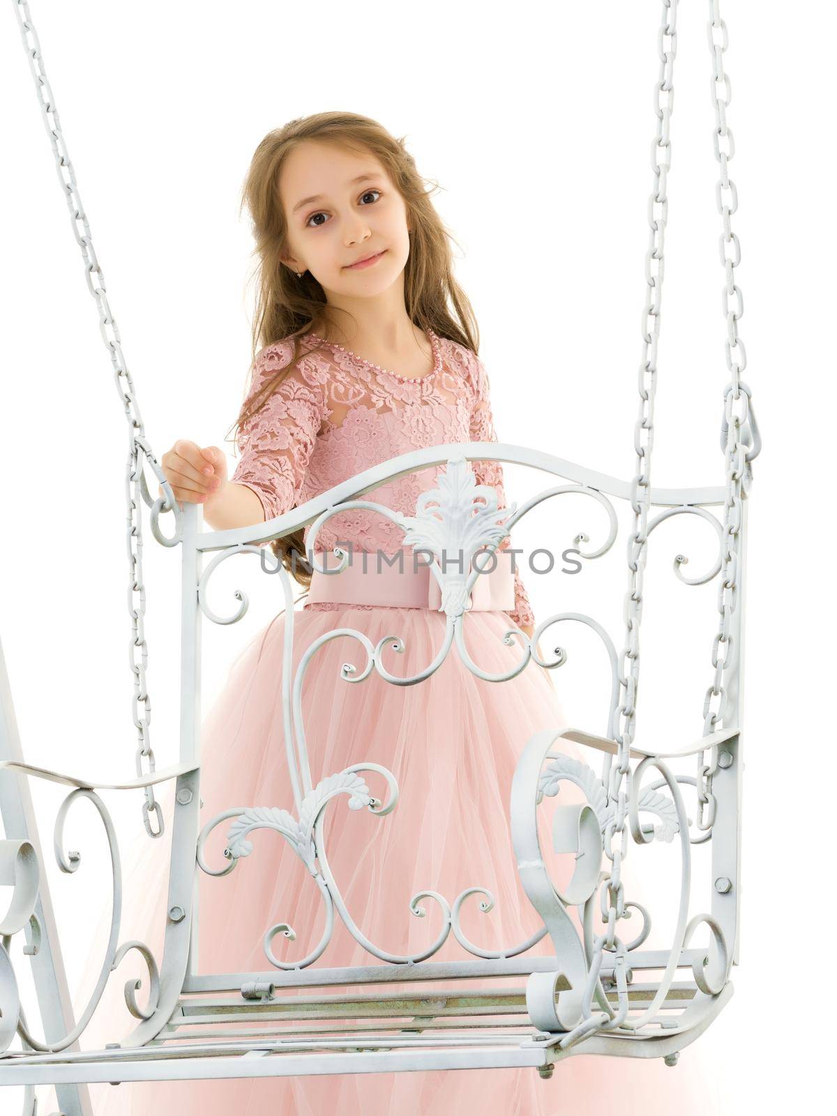 Beautiful girl standing next to an elegant metal swing on a white background, portrait of a beautiful girl in a magnificent dress, seriously looking at the camera
