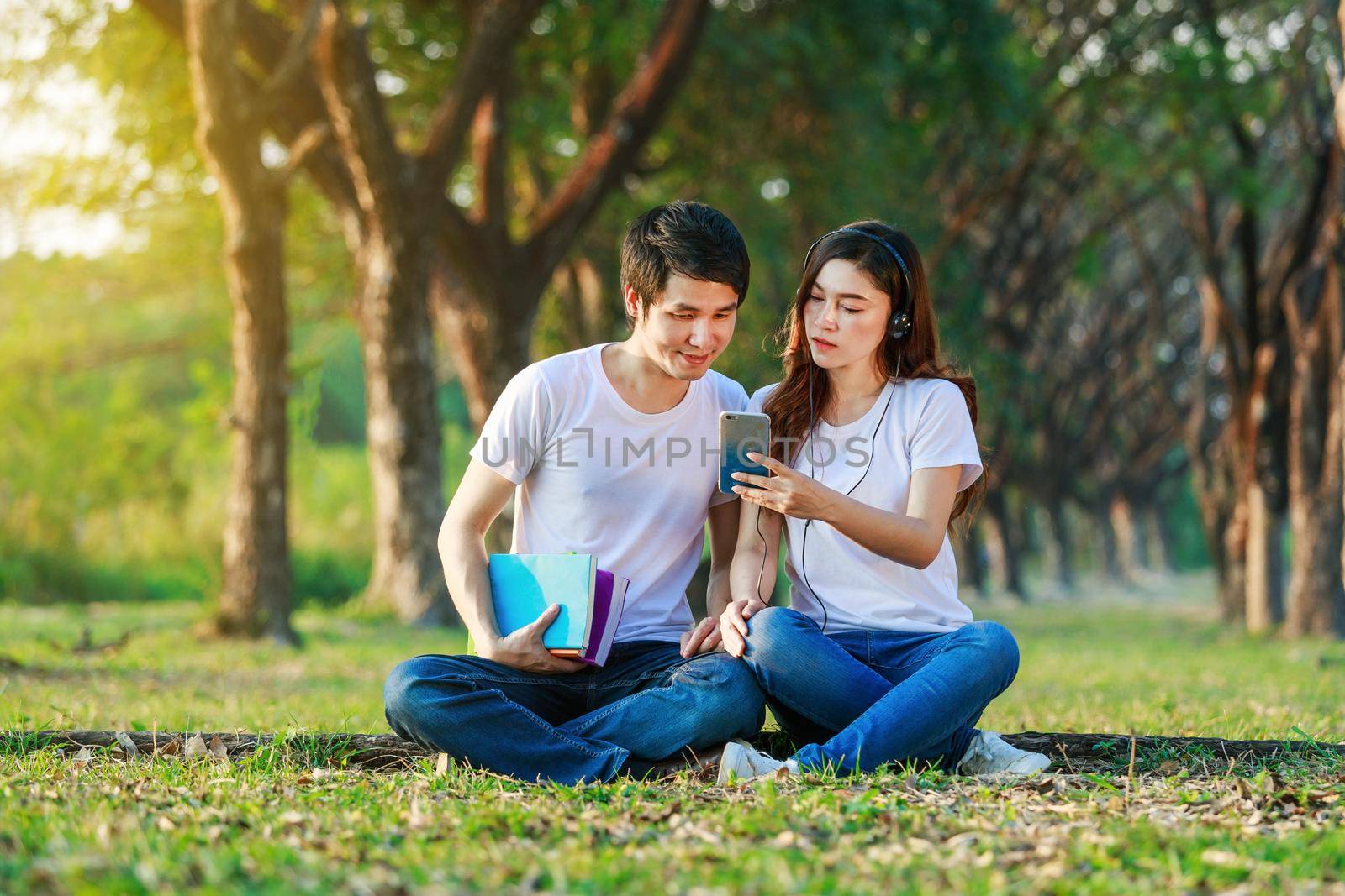 young couple listening music from mobile with headphone in the park