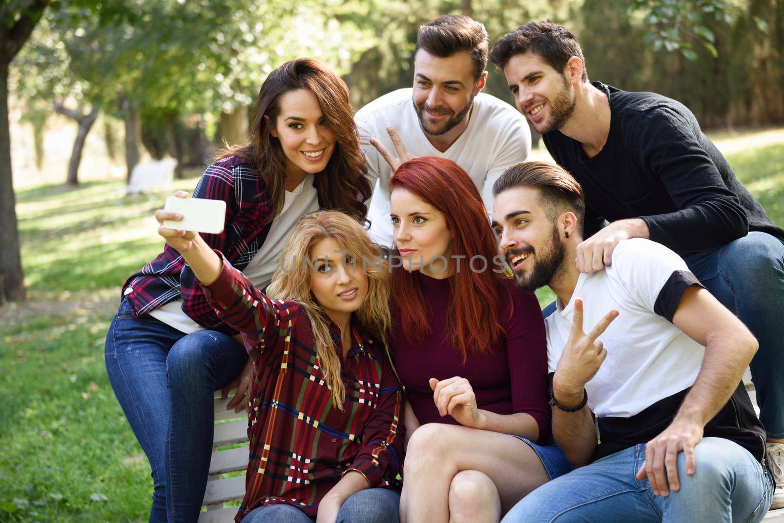 Group of friends taking selfie in urban park. Five young people wearing casual clothes.
