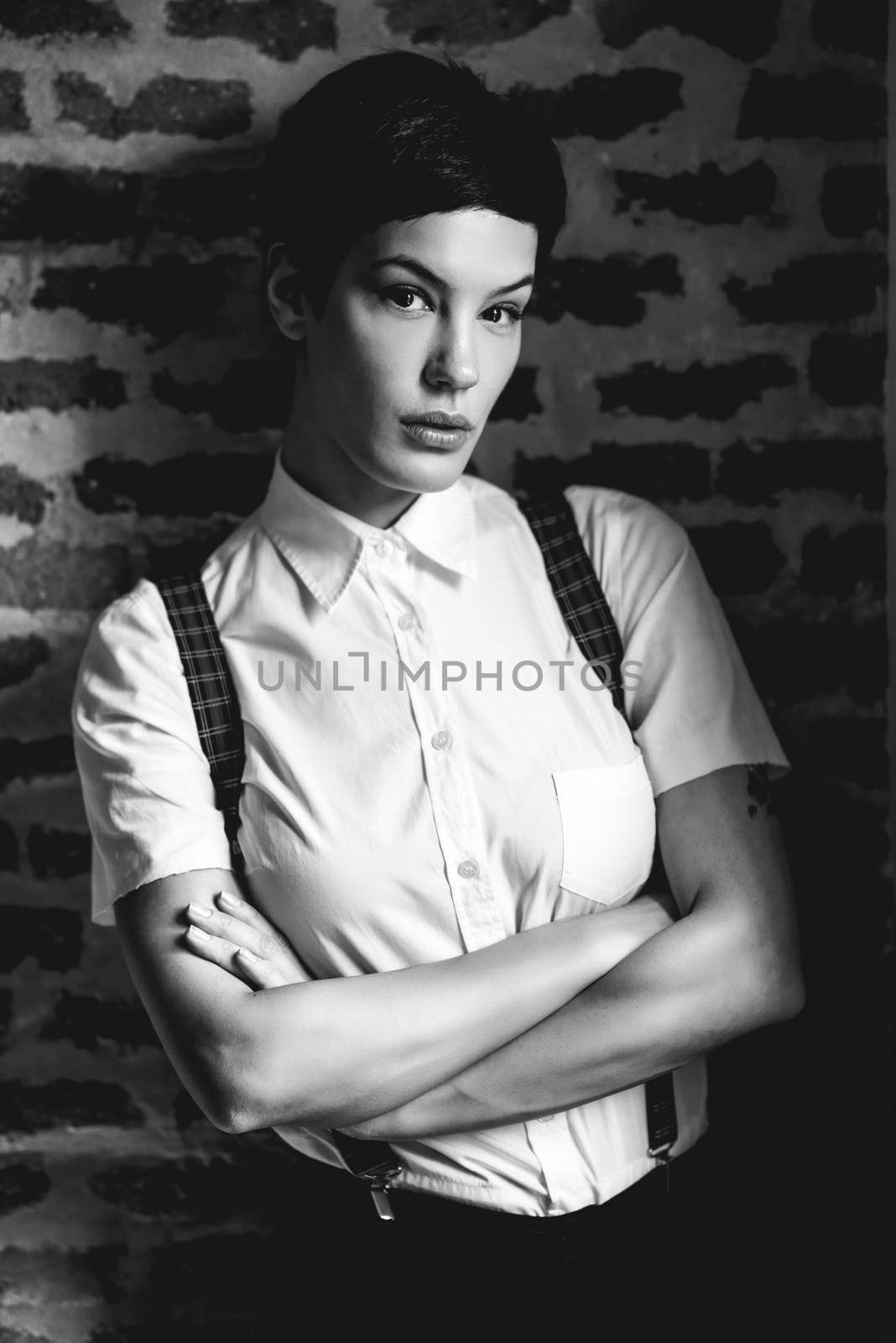 Beautiful young woman, model of fashion, with very short haircut, looking at camera with a brick wall in the background. Beauty and hairstyles concept.