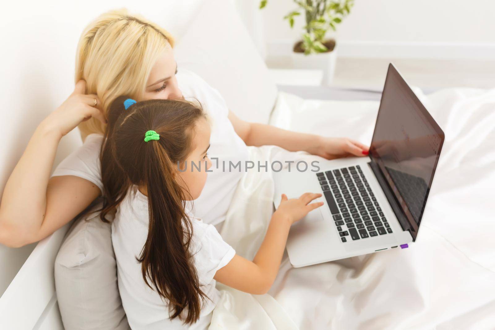 Smiling mother and daughter using laptop in bed at home by Andelov13