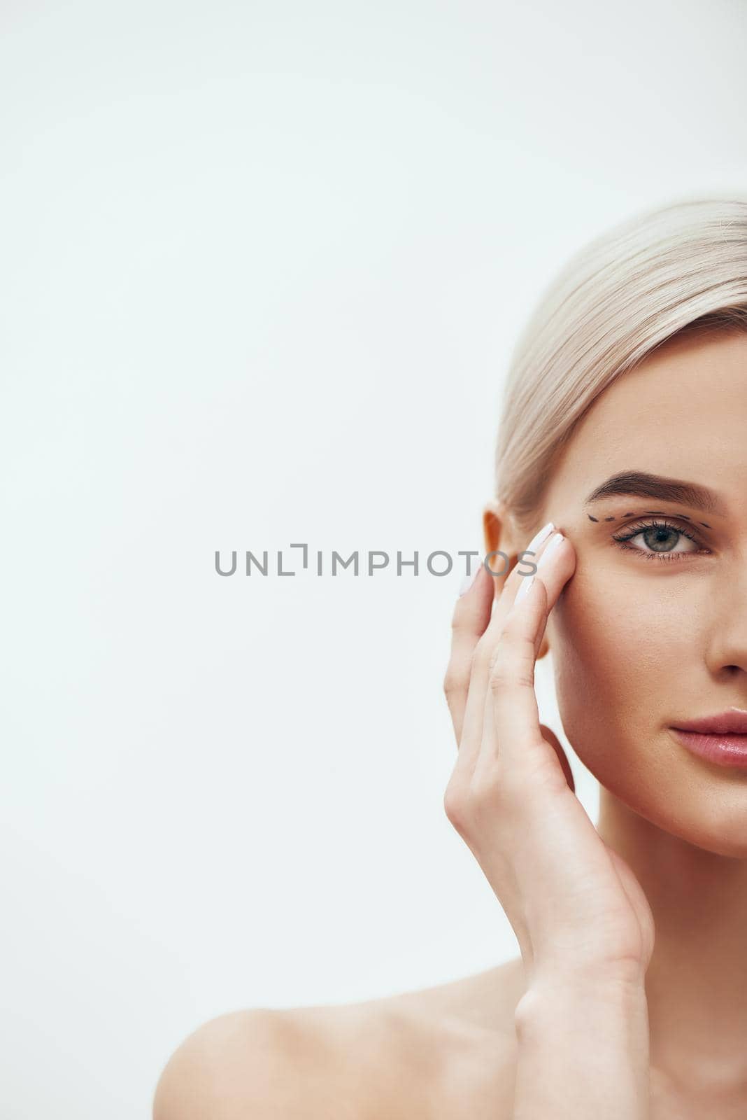 Plastic Surgery Operation. Cropped photo of pretty and young blonde woman touching her face with black surgical lines on eyelids and looking at camera by friendsstock