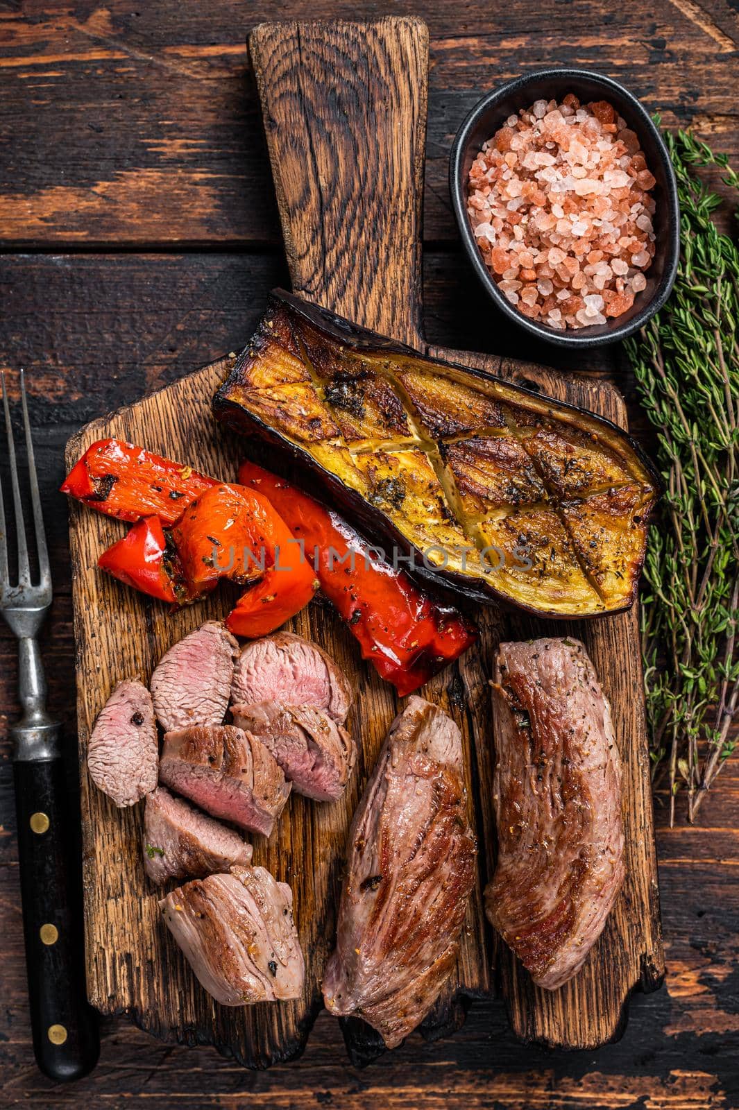 Roasted lamb tenderloin Fillet Meat steak on wooden cutting board. Dark wooden background. Top view.