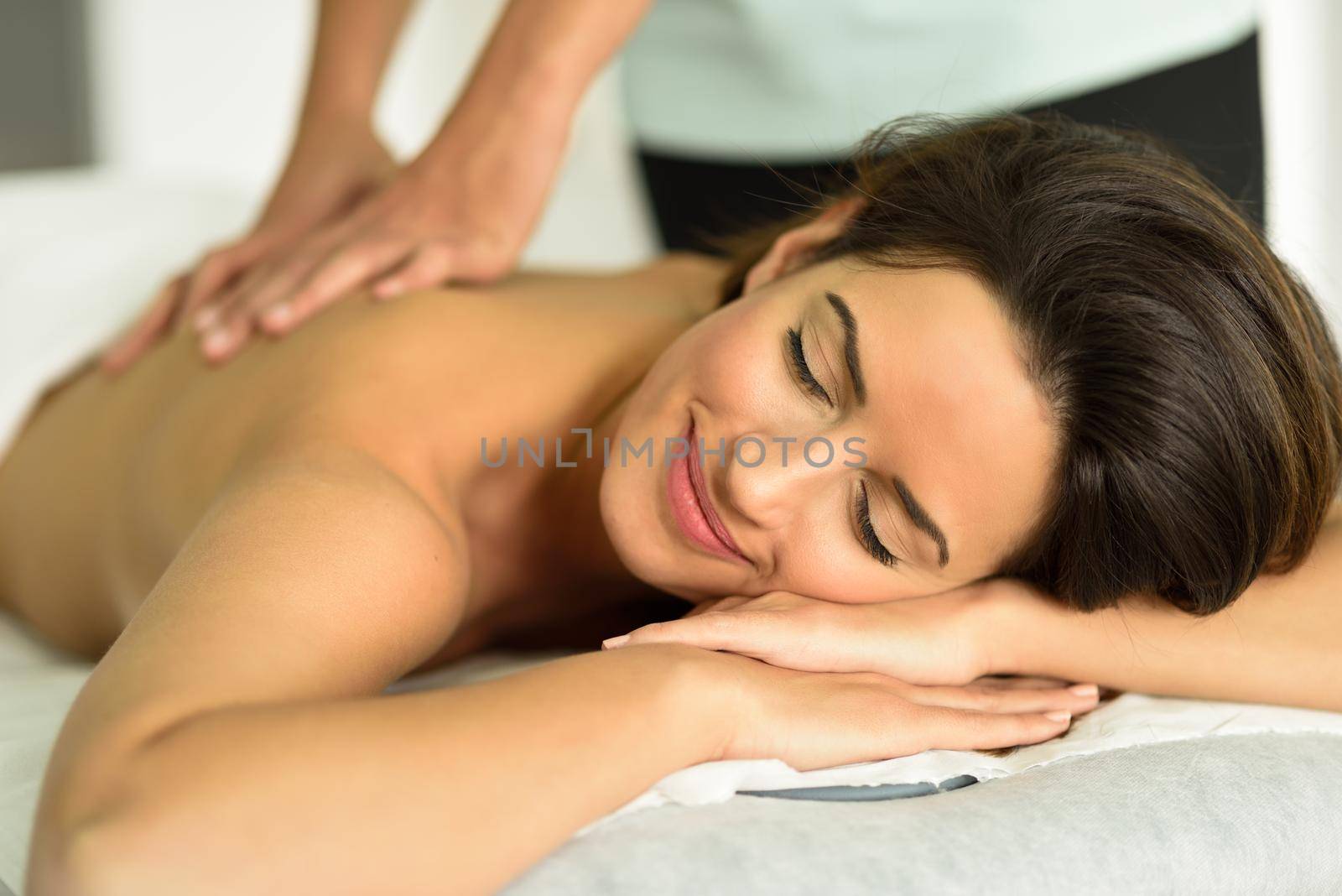 Young female receiving a relaxing back massage in a spa center. Brunette woman patient is receiving treatment by professional therapist.